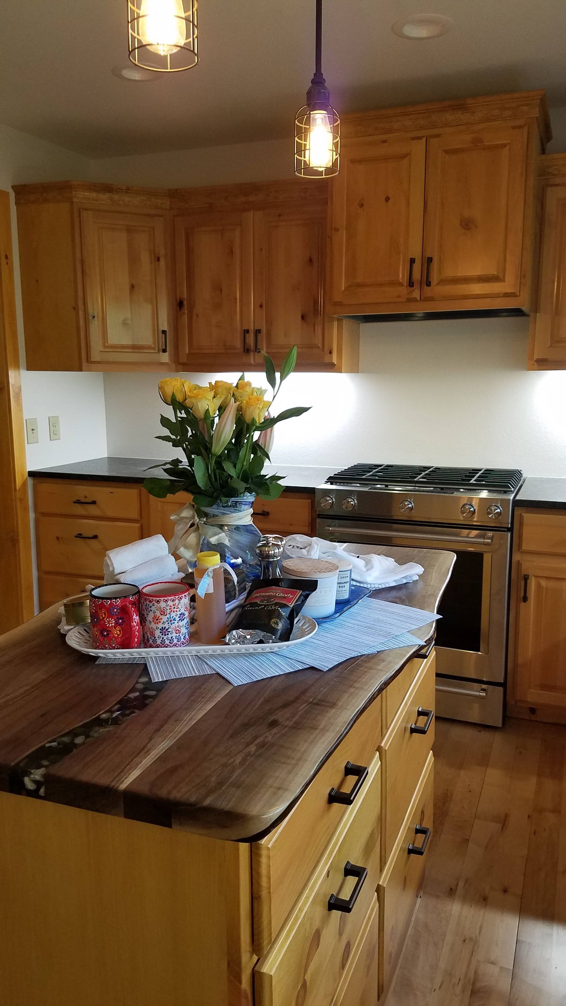 Warm kitchen with wooden cabinets, island centerpiece, flowers, and hanging pendant lights.