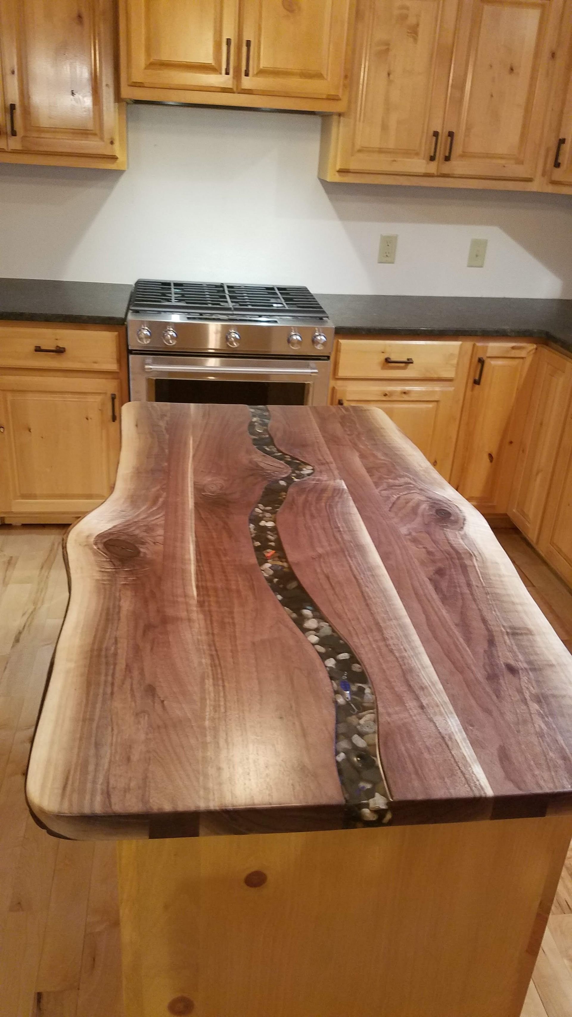 Rustic live-edge wooden table with resin inlay in a kitchen with wood cabinets and a stove in the background