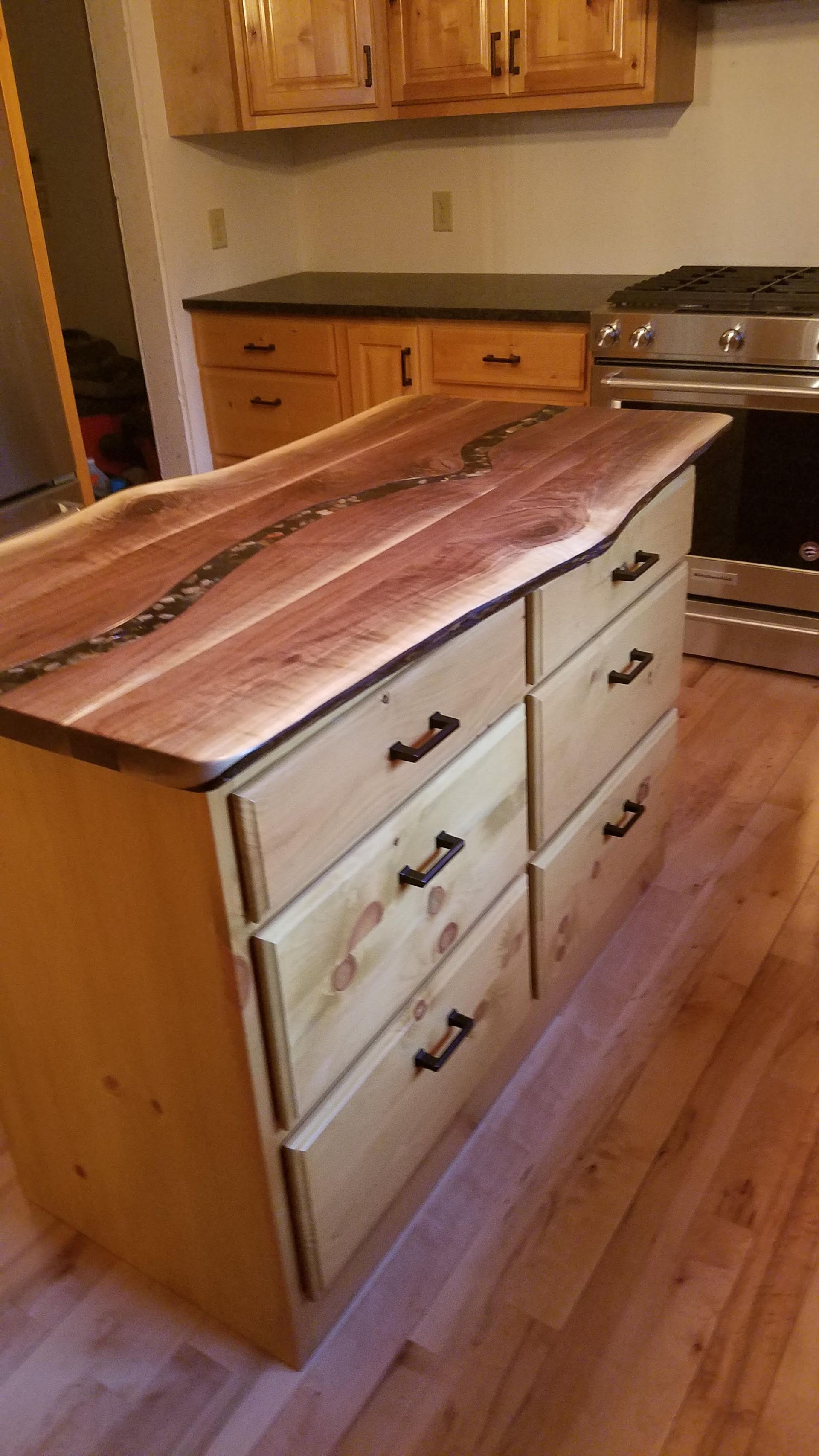 Kitchen island with butcher-block top and white drawers on a hardwood floor, in a wood-paneled kitchen