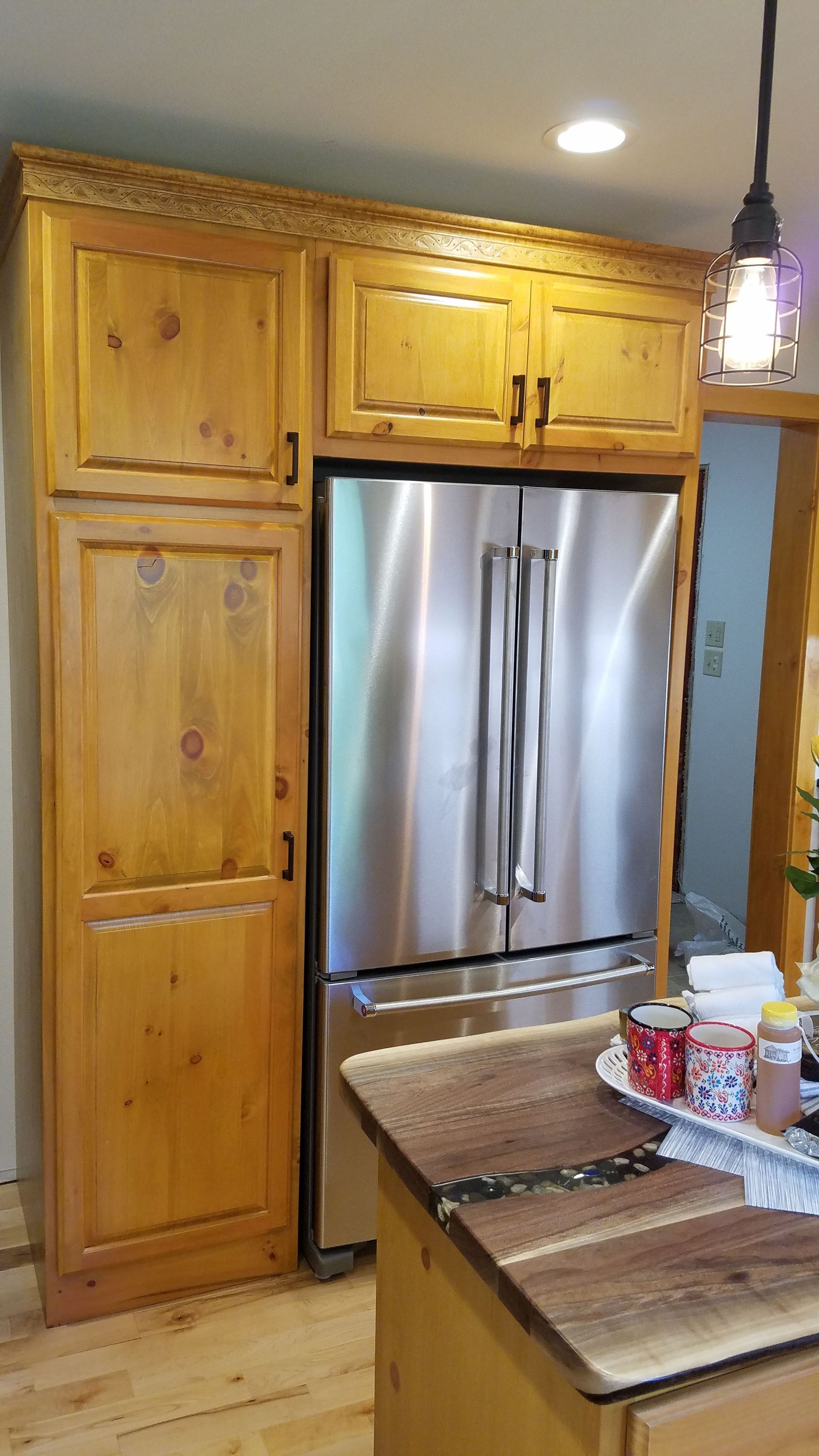 Kitchen with stainless steel refrigerator, wooden cabinets, and a granite island with items on top