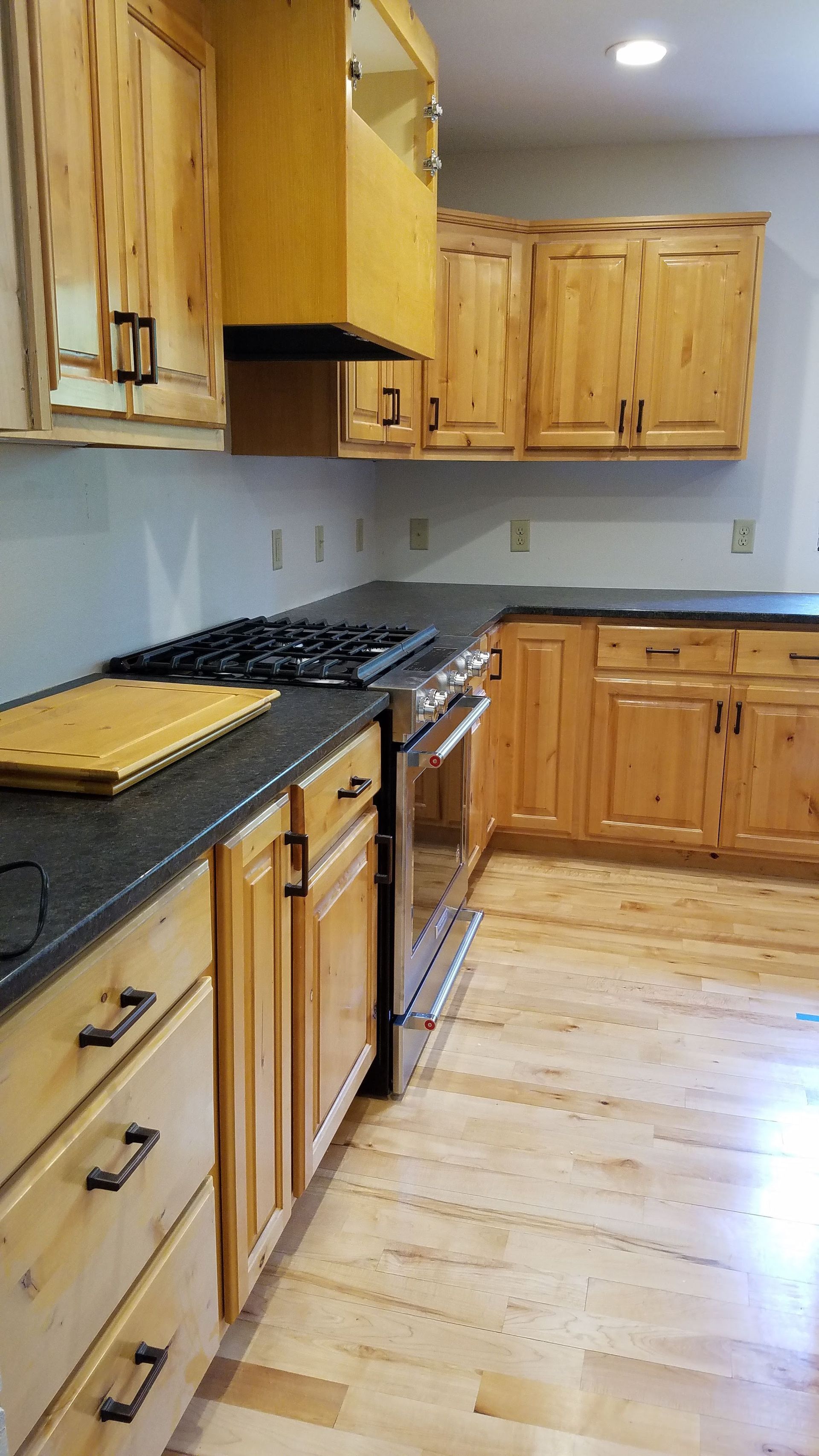 Wooden kitchen with black countertops, gas stove, and light hardwood floor