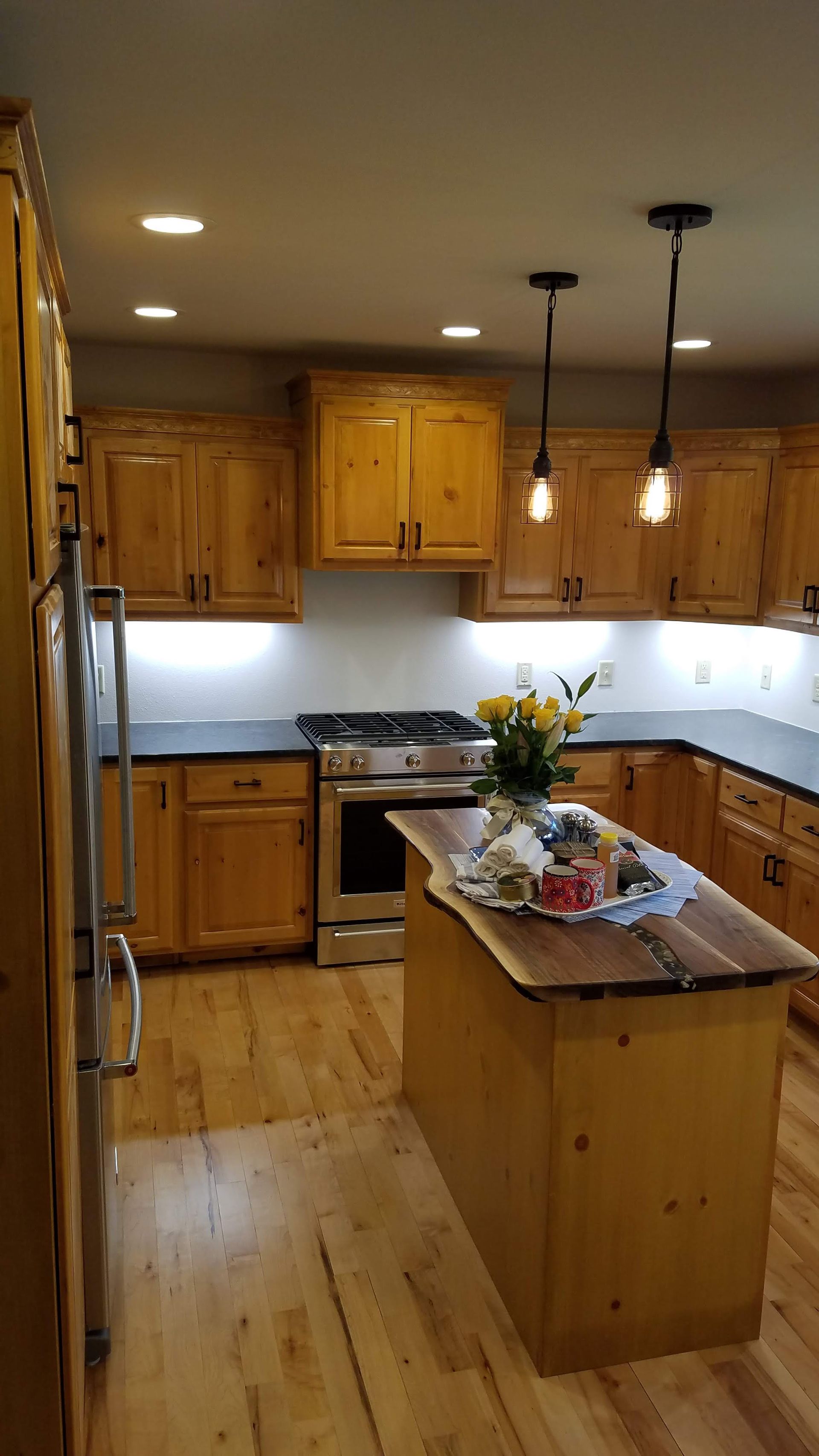 Warm wood kitchen with island, stainless stove, pendant lights, and flowers on the counter.