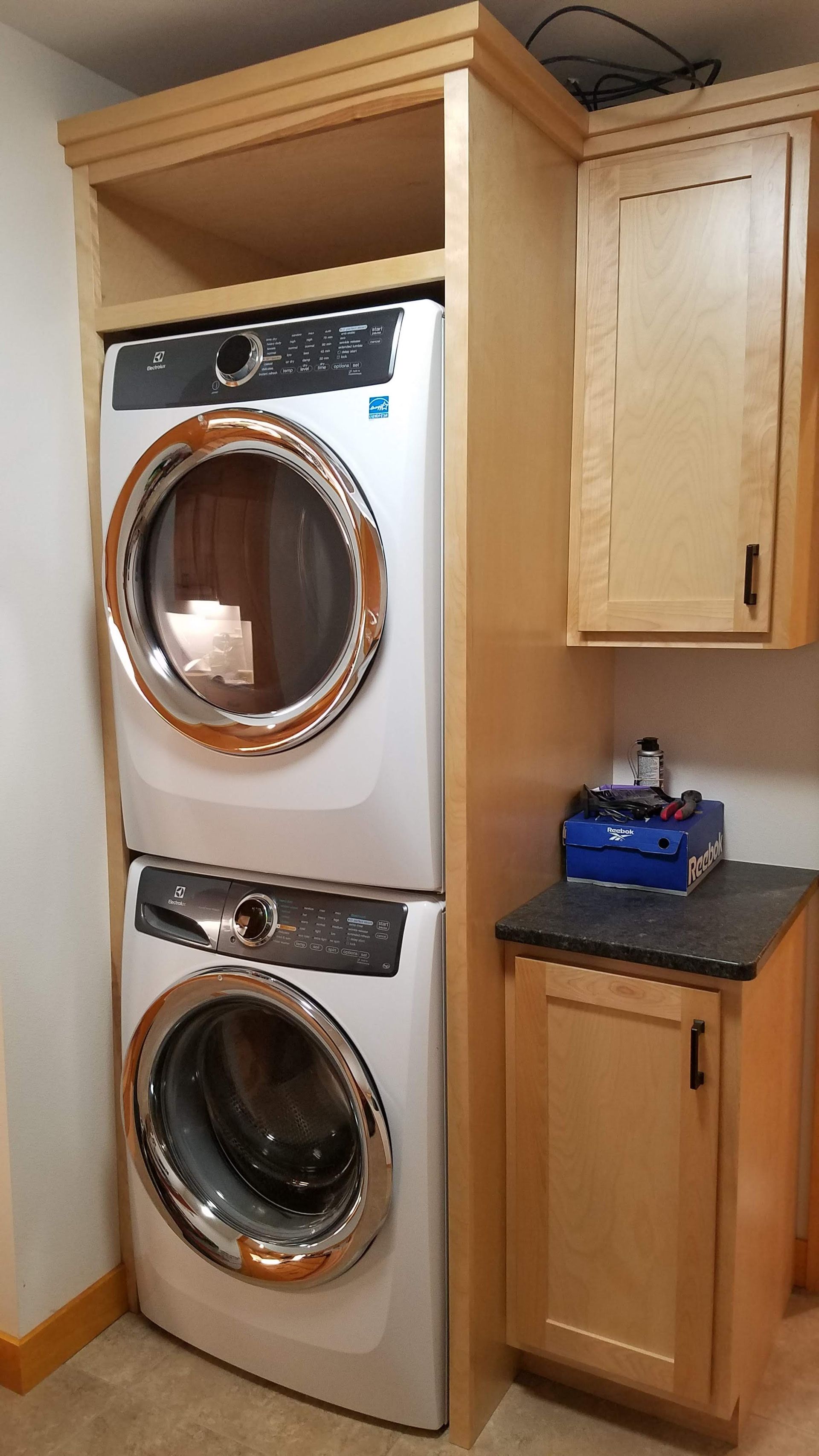 Stacked washer and dryer in a laundry nook with wood cabinets and dark countertop