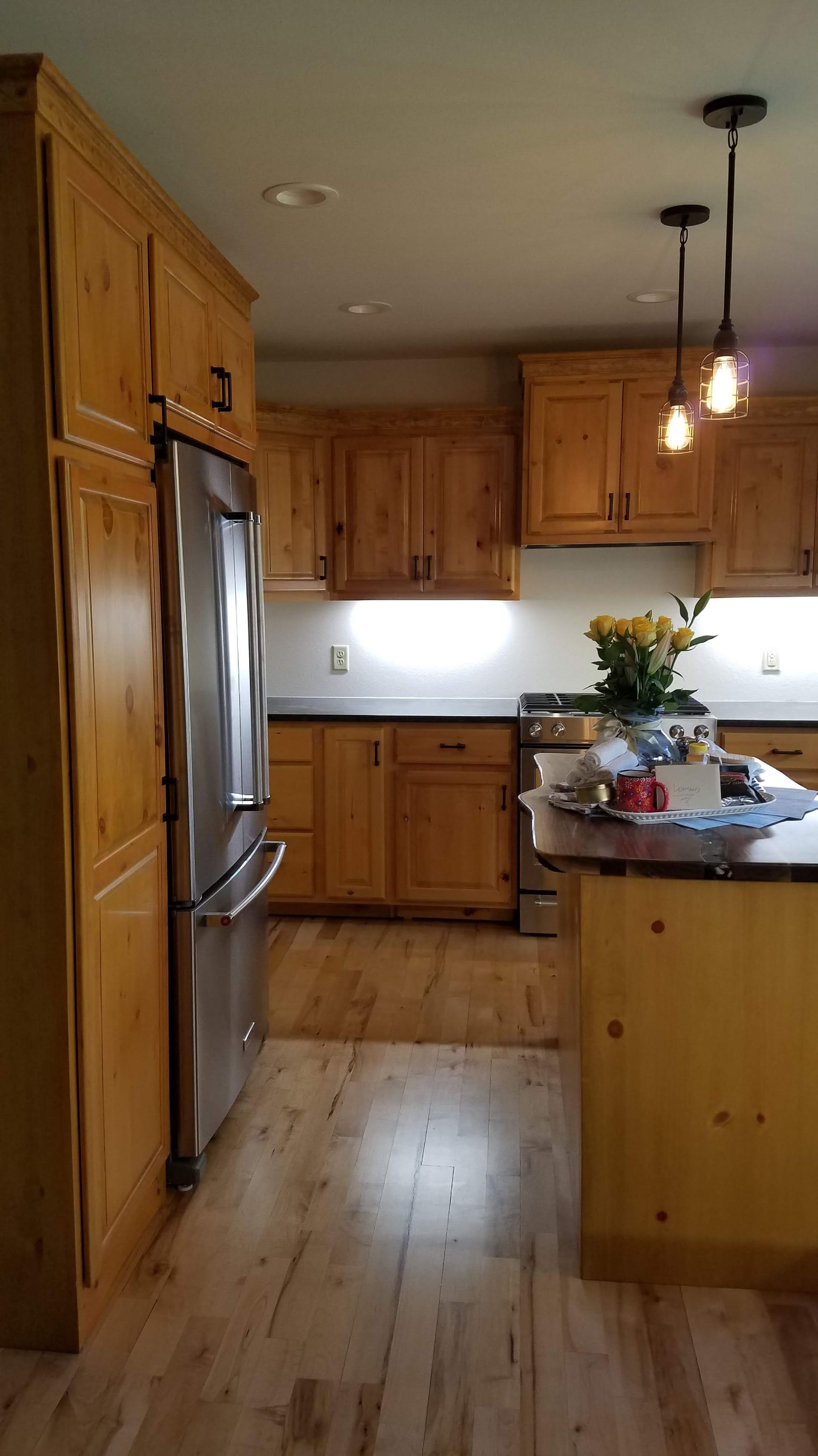 Wooden kitchen with stainless steel refrigerator, center island, and pendant lights by a bright window.