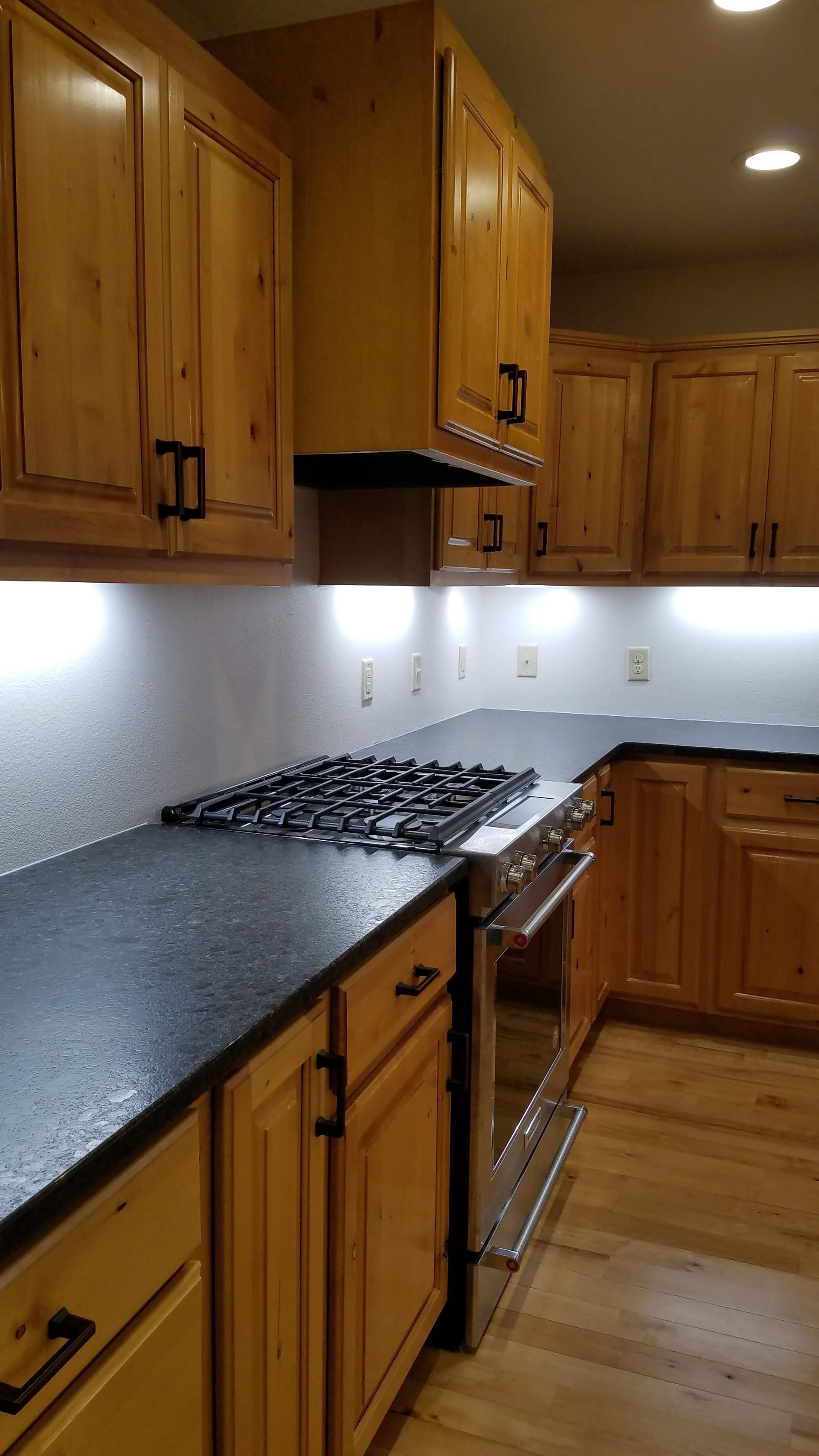 Modern kitchen with wooden cabinets, black countertop, gas range, and under-cabinet lighting