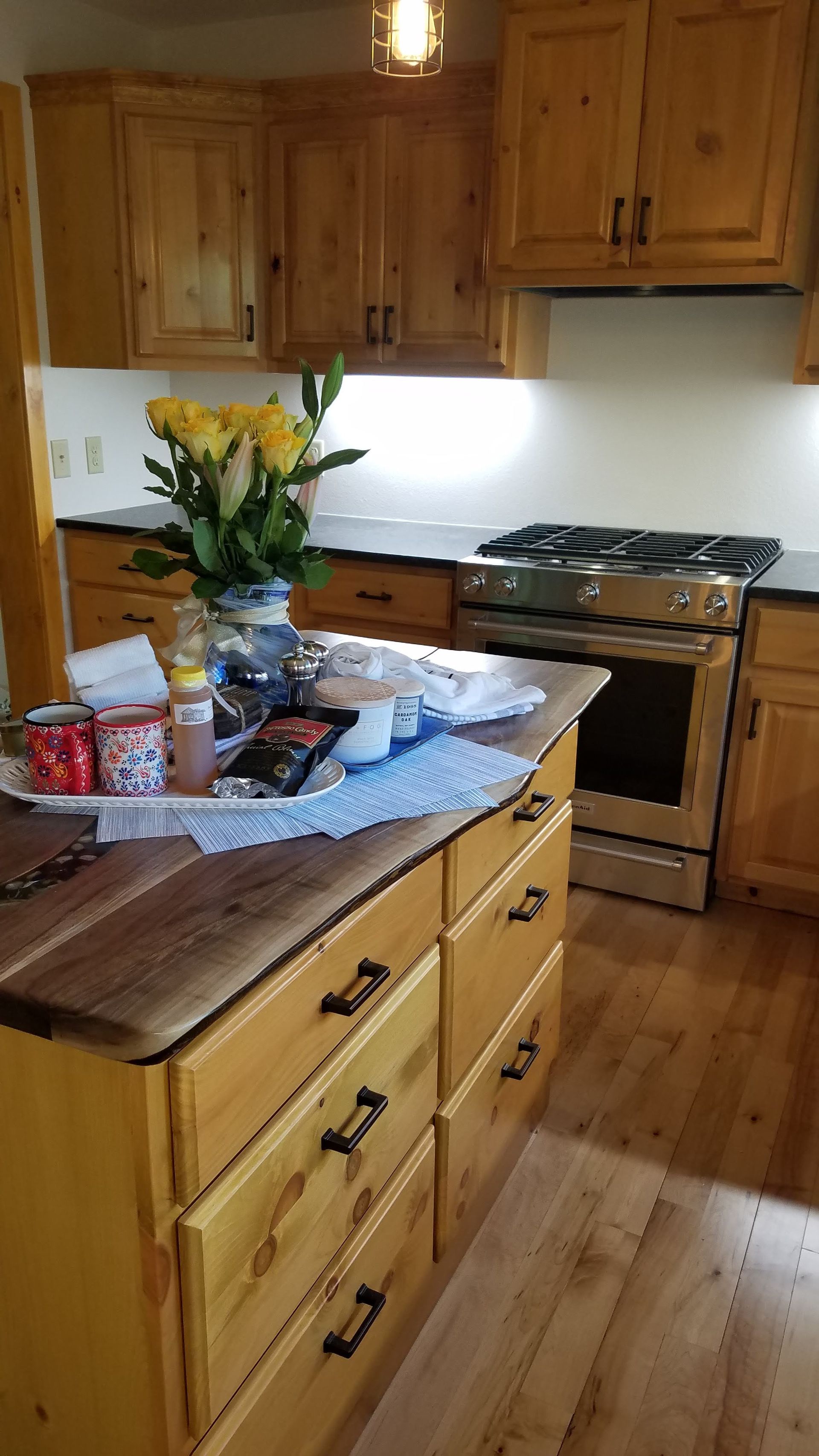 Cozy kitchen with wooden cabinets, island, flowers, and a stove under bright light.