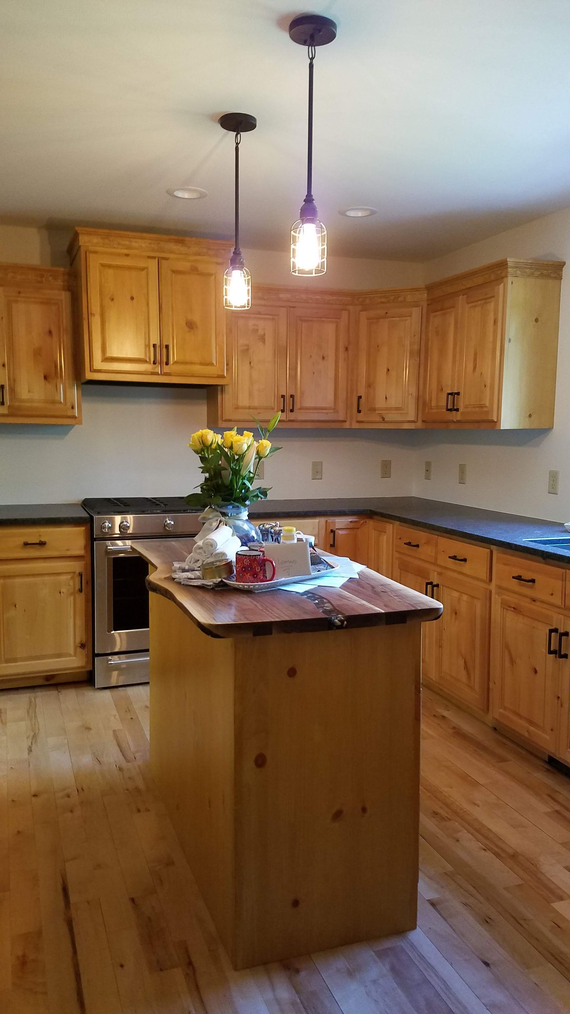 Wooden kitchen with island, hanging lights, and a vase of flowers on the counter.
