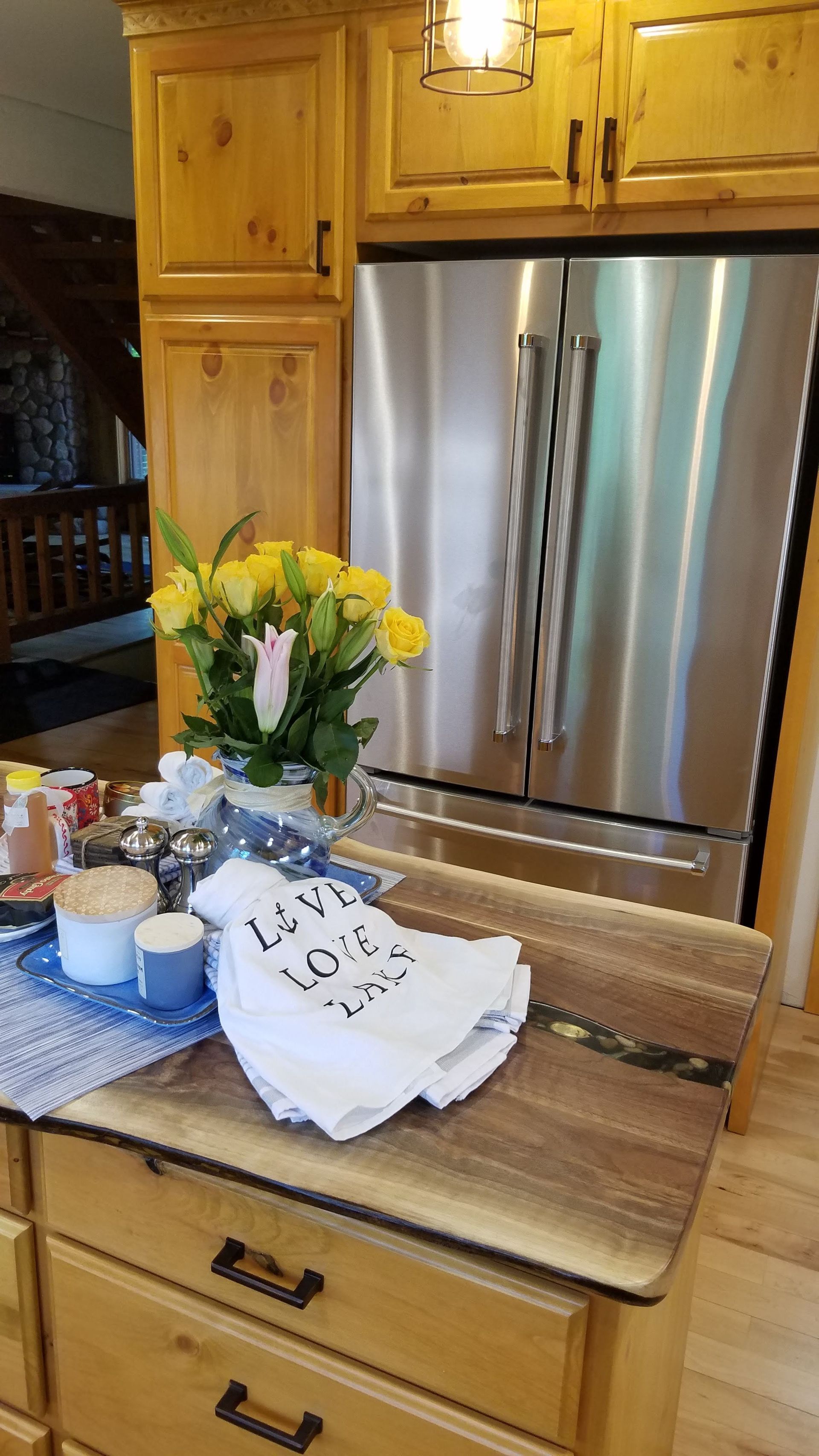 Kitchen counter with flowers, drinks, and a white bag in front of a stainless steel refrigerator.