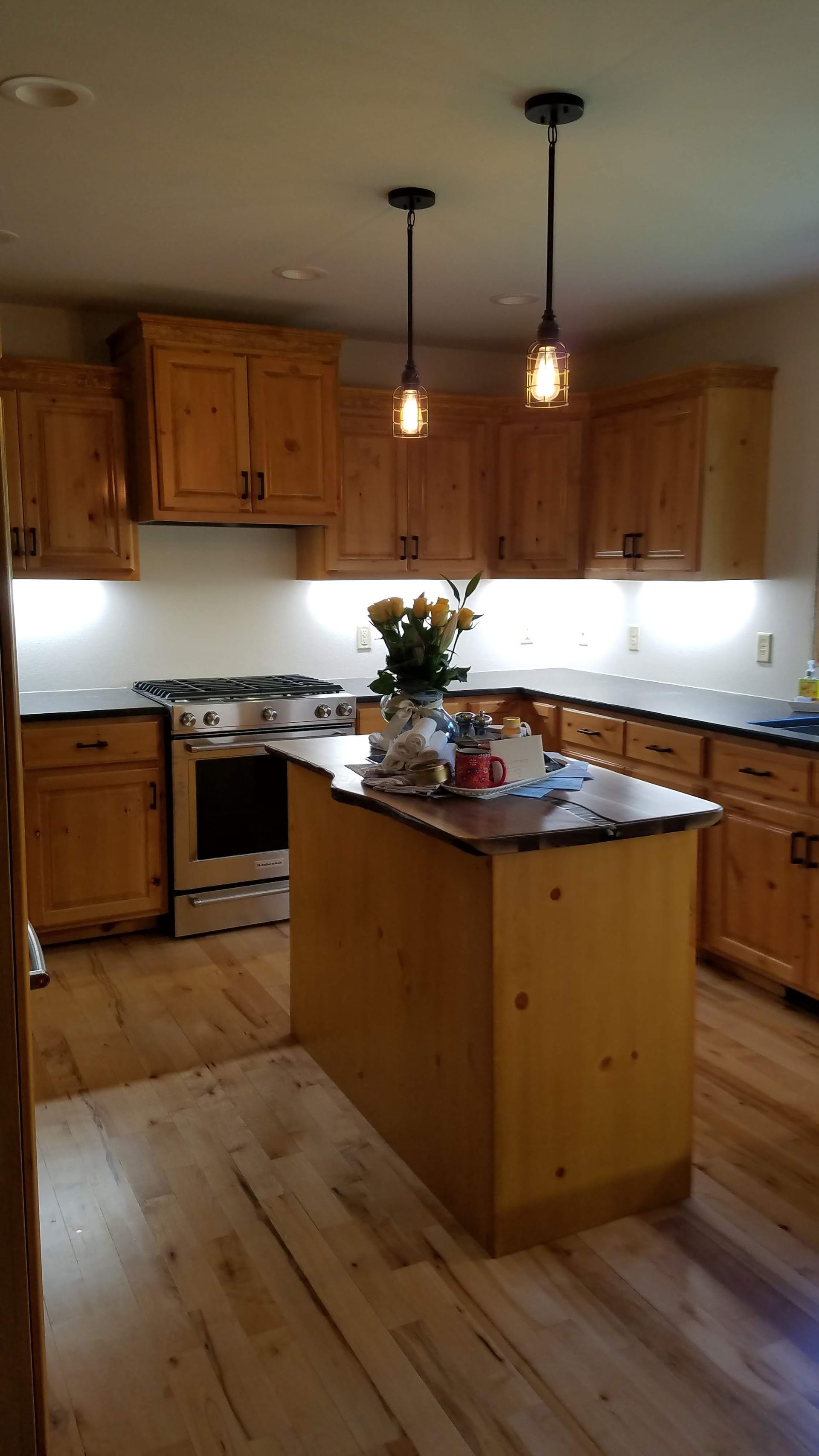 Warm wood kitchen with central island, pendant lights, cabinets, and a vase of flowers on the counter.