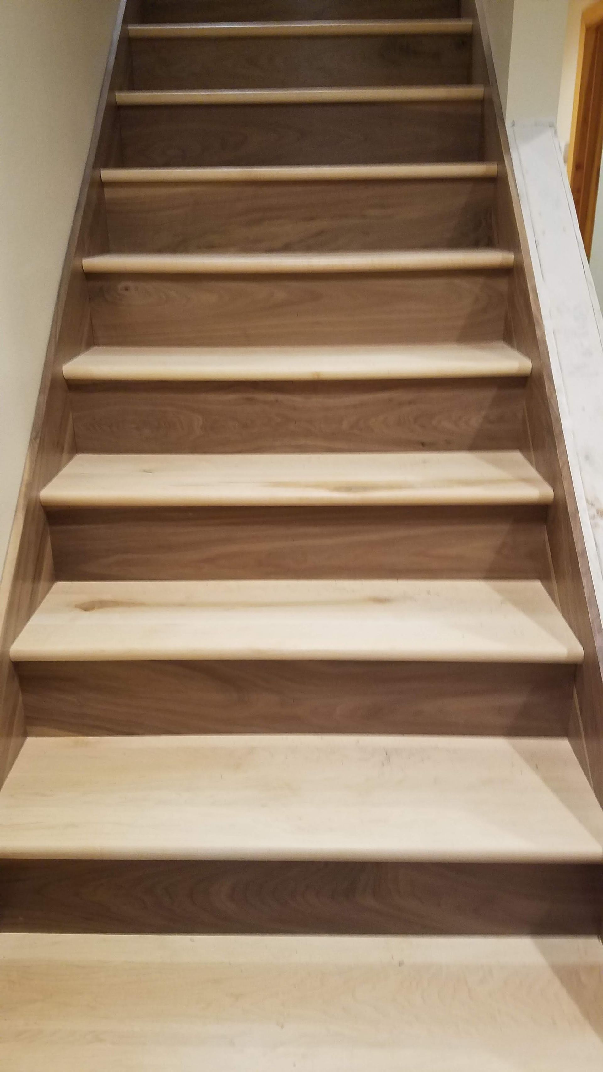 Wooden staircase with beige carpeted steps and a white wall on the right
