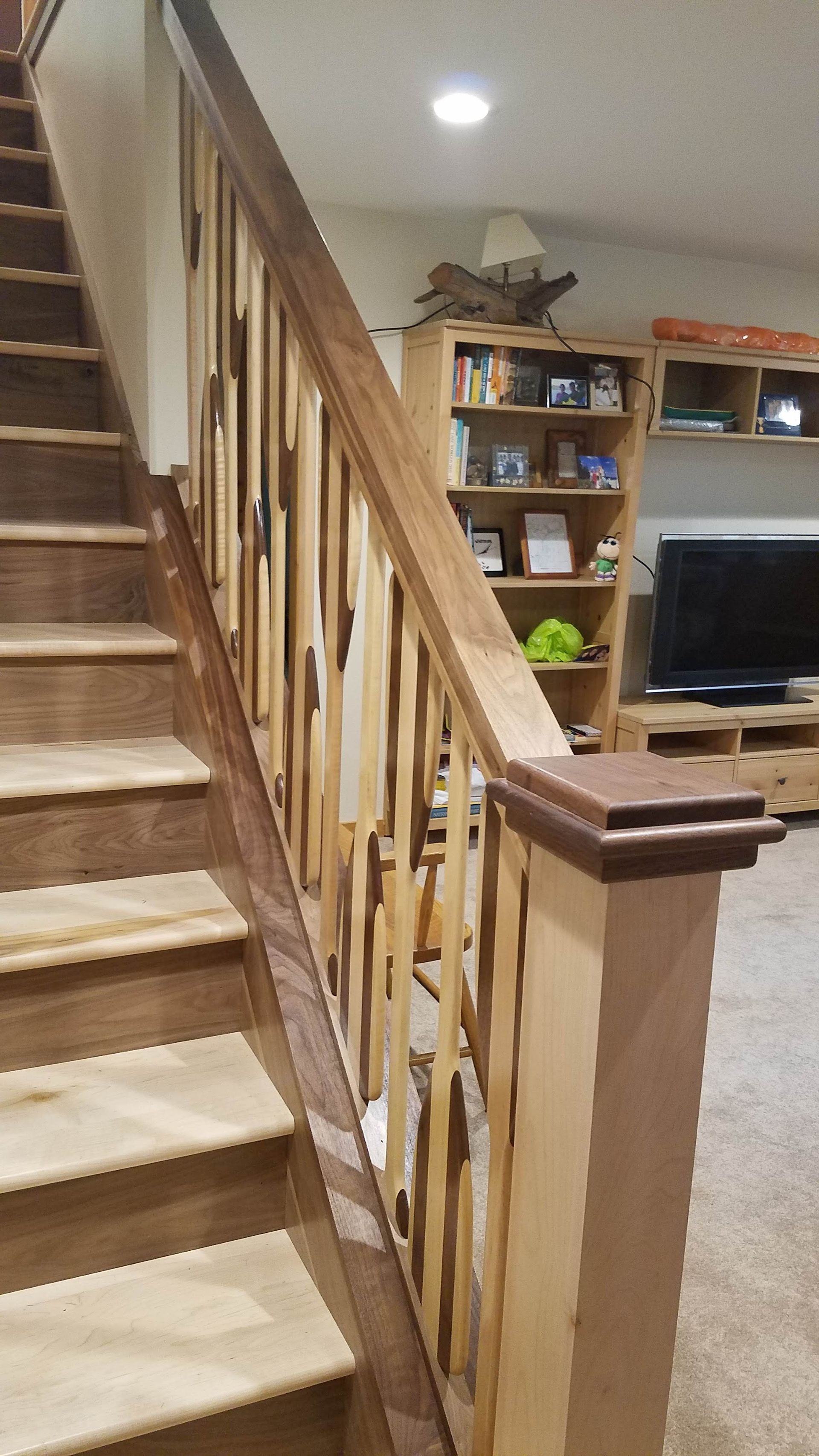 Indoor staircase with wooden railing beside a carpeted living room and TV area