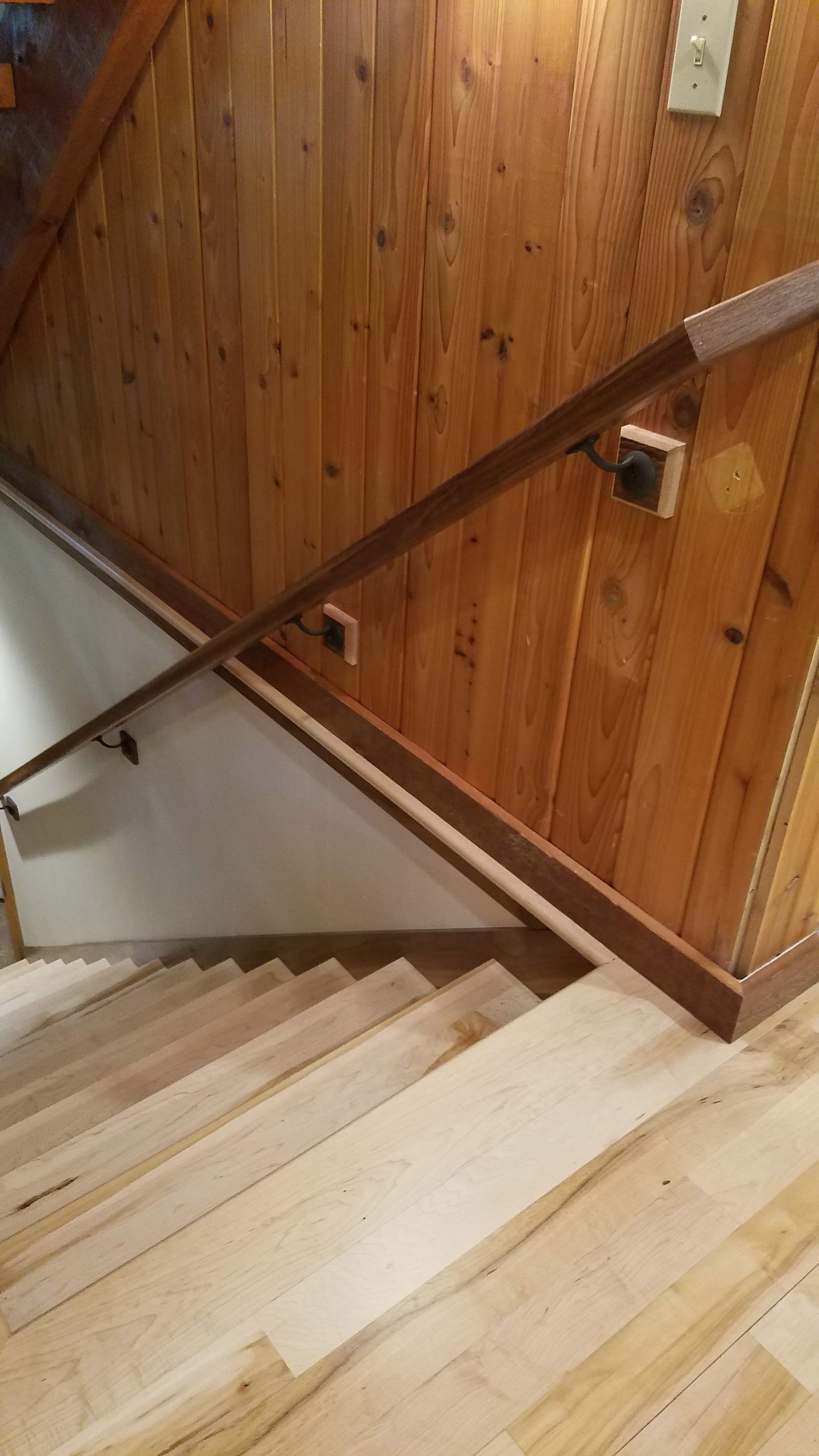 Wood-paneled stairwell with white steps and a dark handrail along the wall