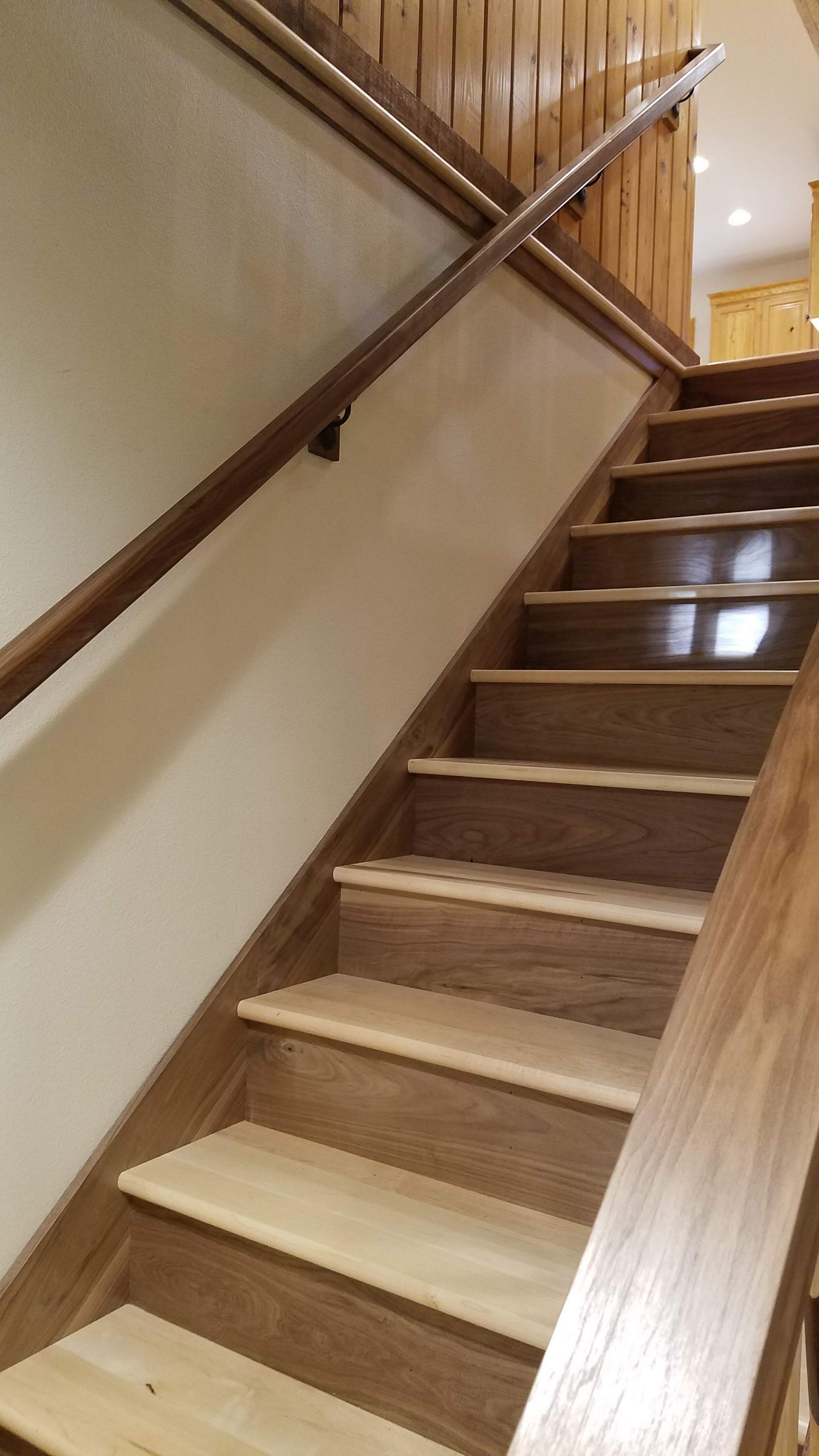 Wooden indoor staircase with banister and beige walls, viewed from the bottom looking up