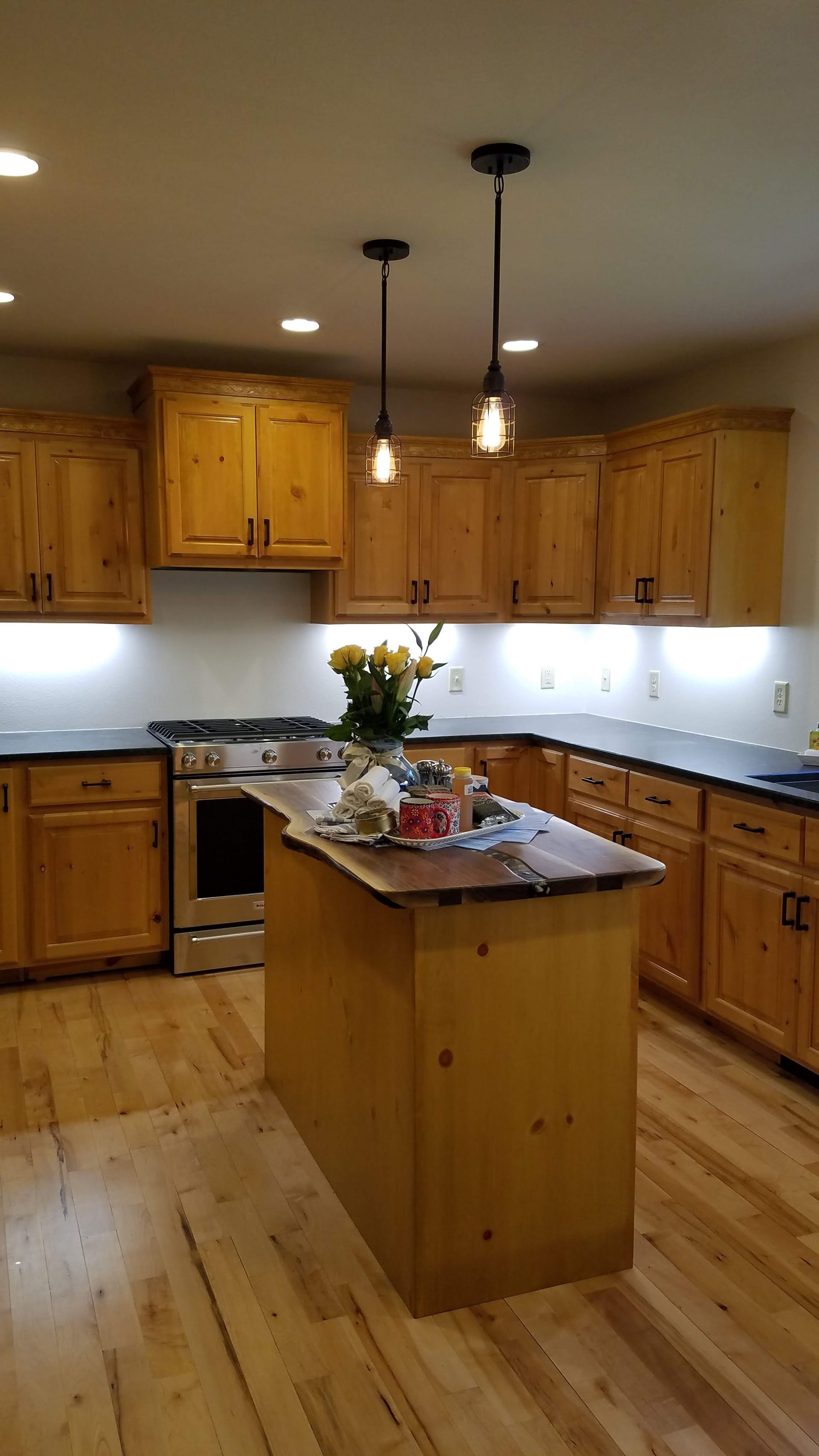 Warm wooden kitchen with island, cabinets, hanging pendant lights, and a vase of flowers on the counter.