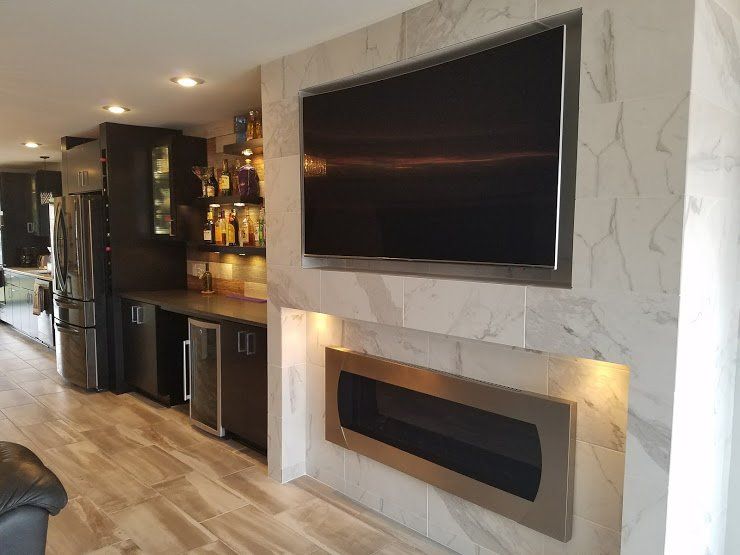 Modern open-concept living room with wall-mounted TV above a marble fireplace and a bar area in the background