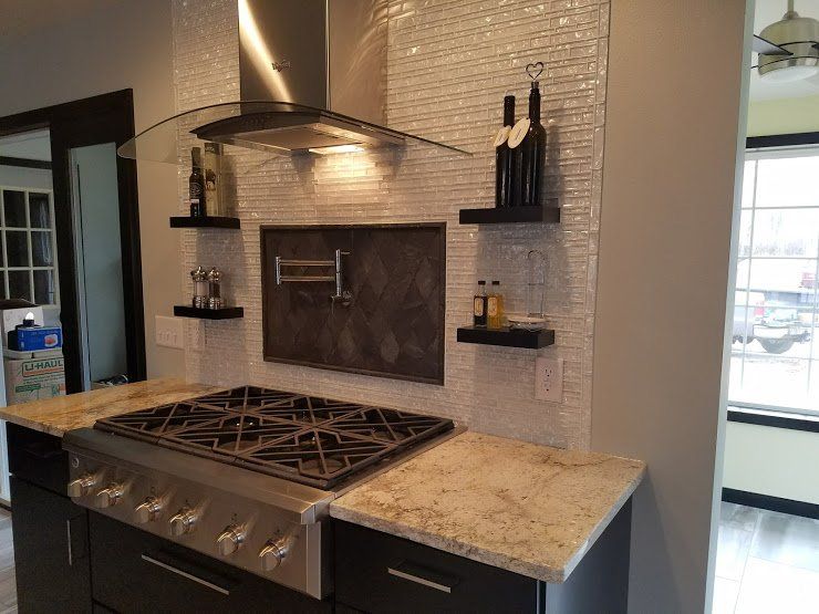 Modern kitchen with stainless steel range, granite countertops, and white tile backsplash near a bright window