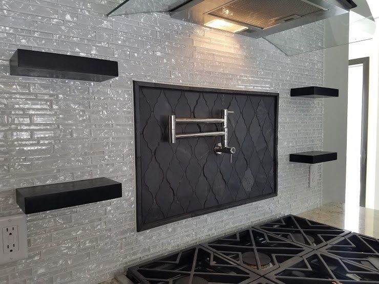 Modern bathroom with gray mosaic tile, black shelves, a towel rack, and a black patterned rug