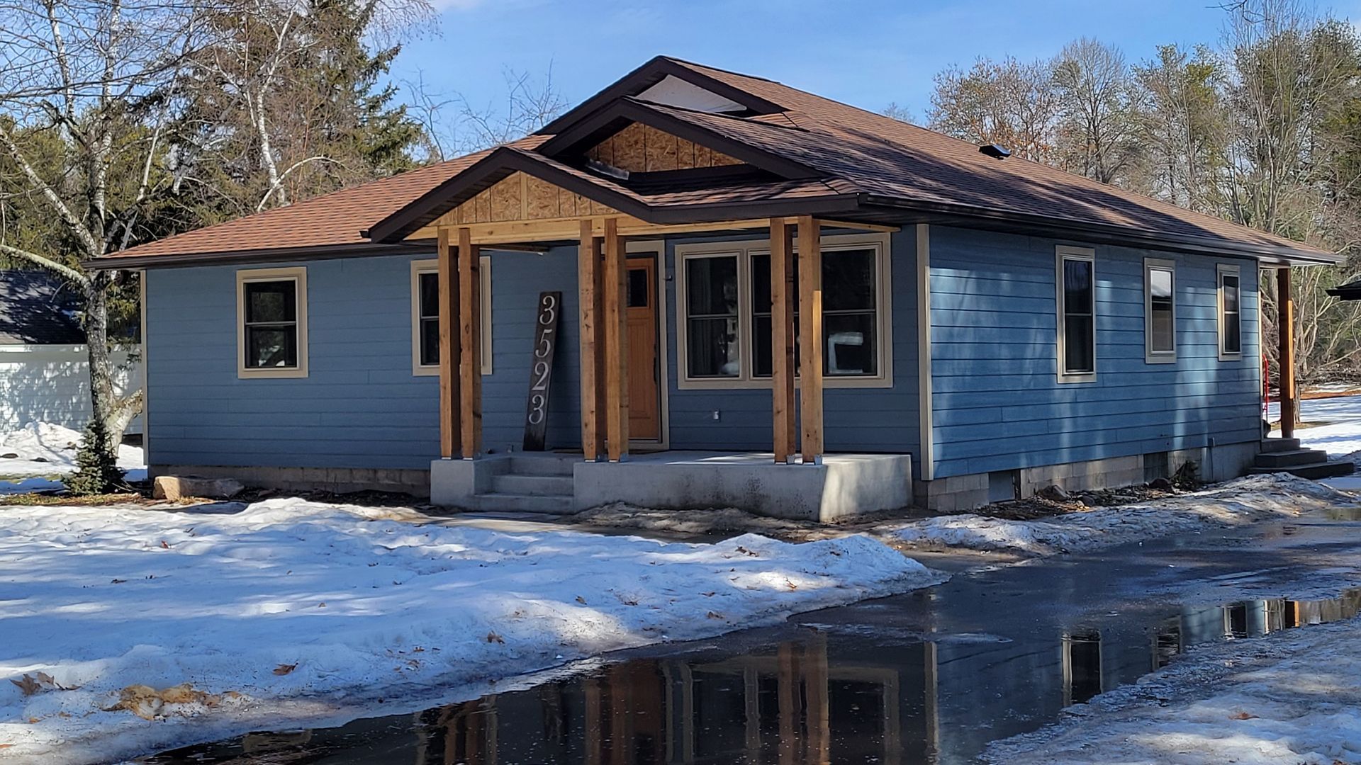 Blue house with wood accents, snow, and a puddle in front.