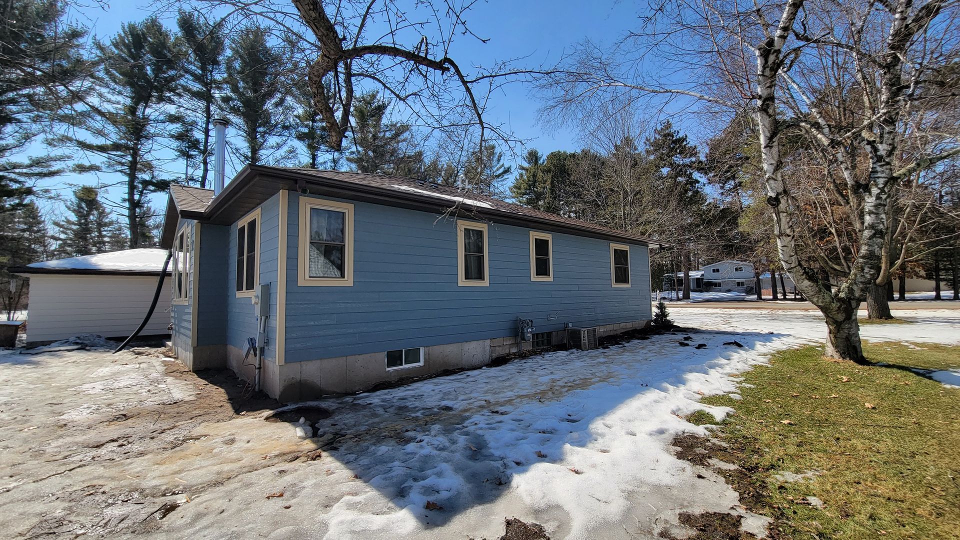 Blue house with snow on the ground, trees in the background, sunny day.