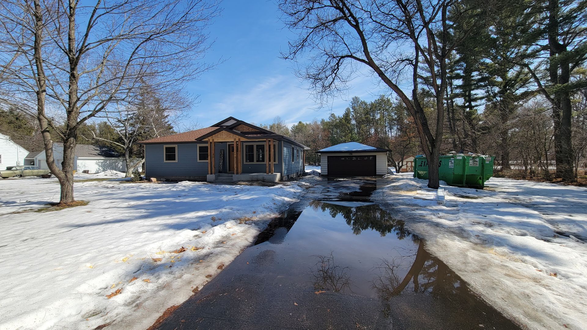 House under construction with snowy surroundings and wet driveway.