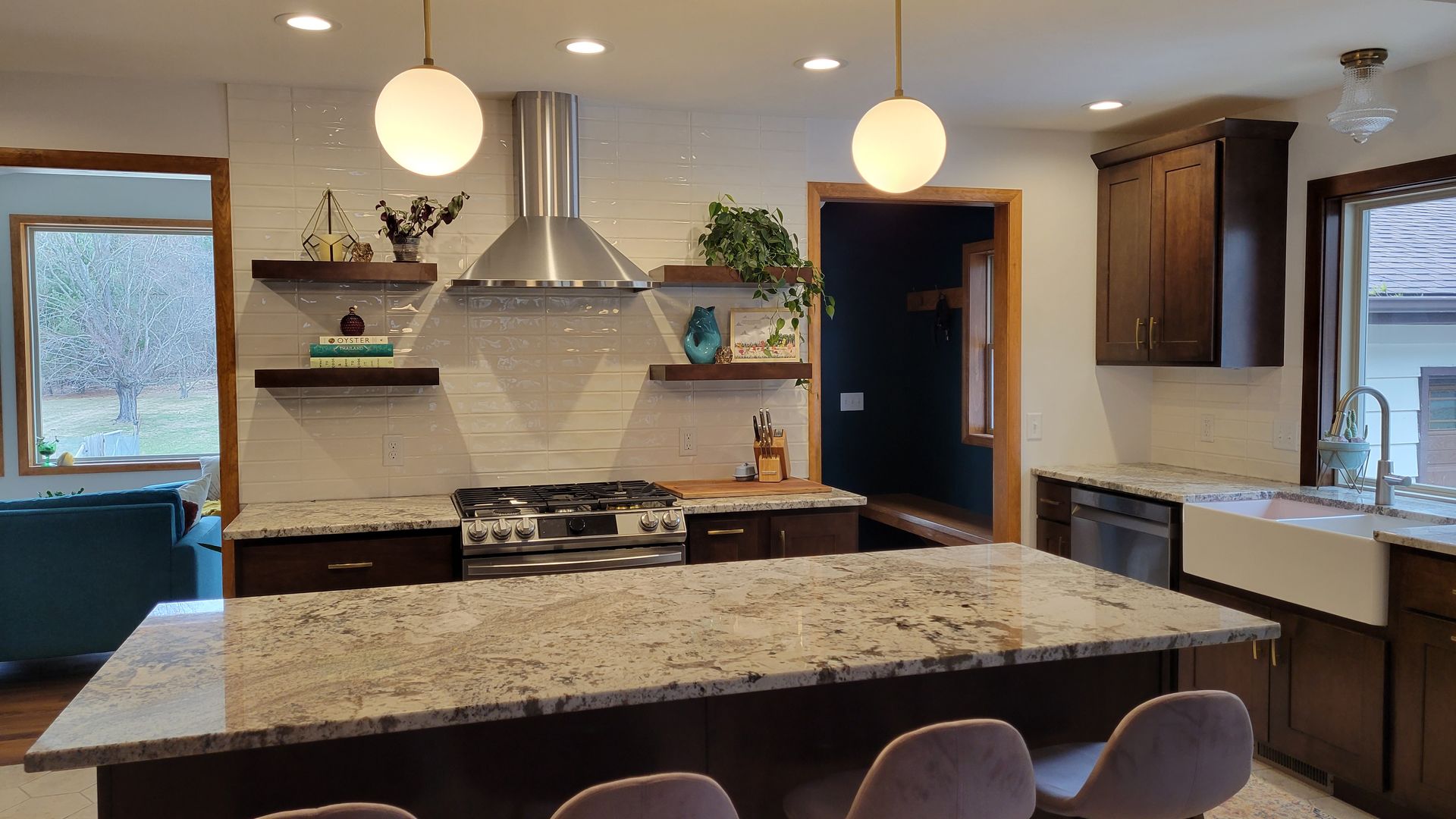 Modern kitchen with dark cabinetry, large island, stainless steel appliances, and two globe pendant lights.