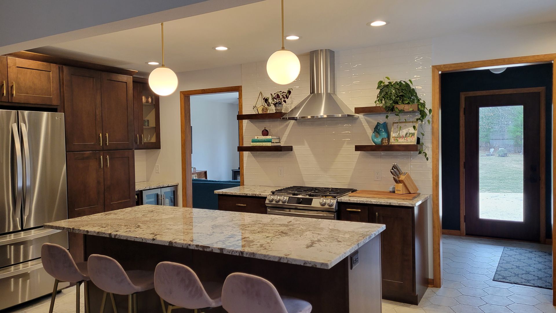 Modern kitchen with island and pendant lights. Stainless steel appliances and dark cabinets, white tiled backsplash.