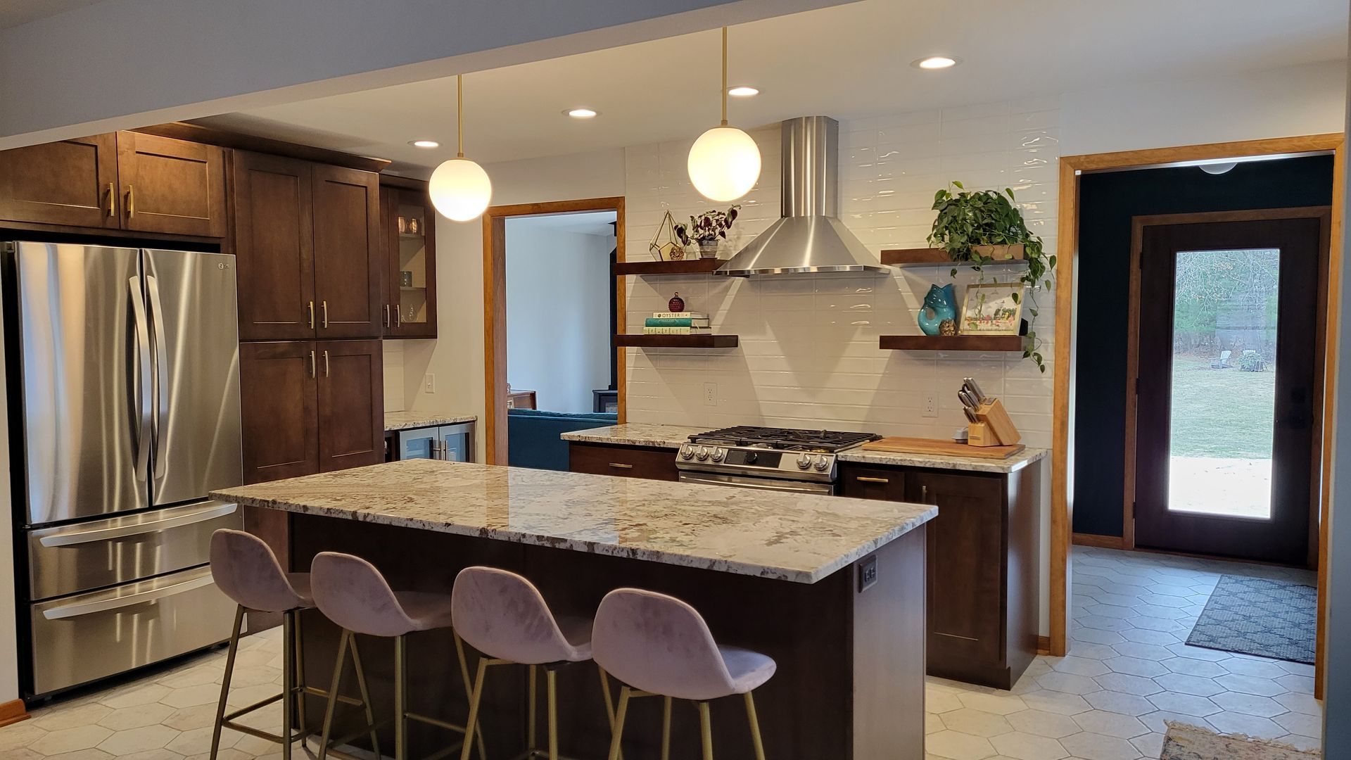 Kitchen with dark wood cabinets, stainless steel appliances, island with pink stools, and globe pendant lights.