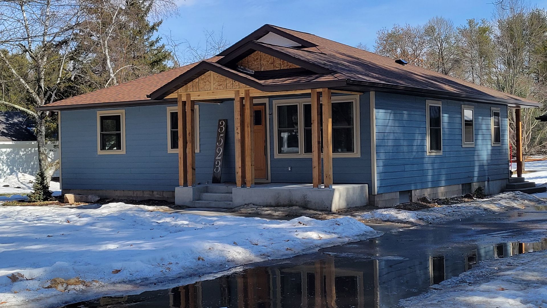 Blue house with brown roof and porch in snowy setting.