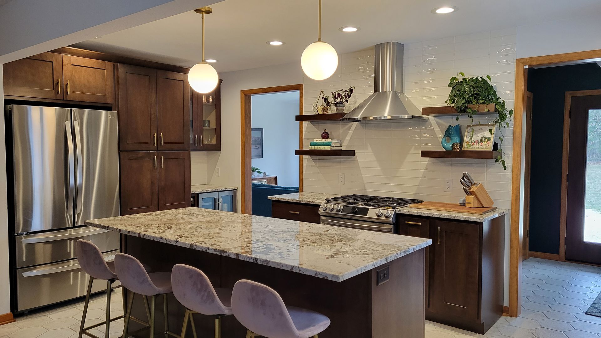 Modern kitchen with island, stainless steel appliances, dark cabinets, and globe pendant lights.