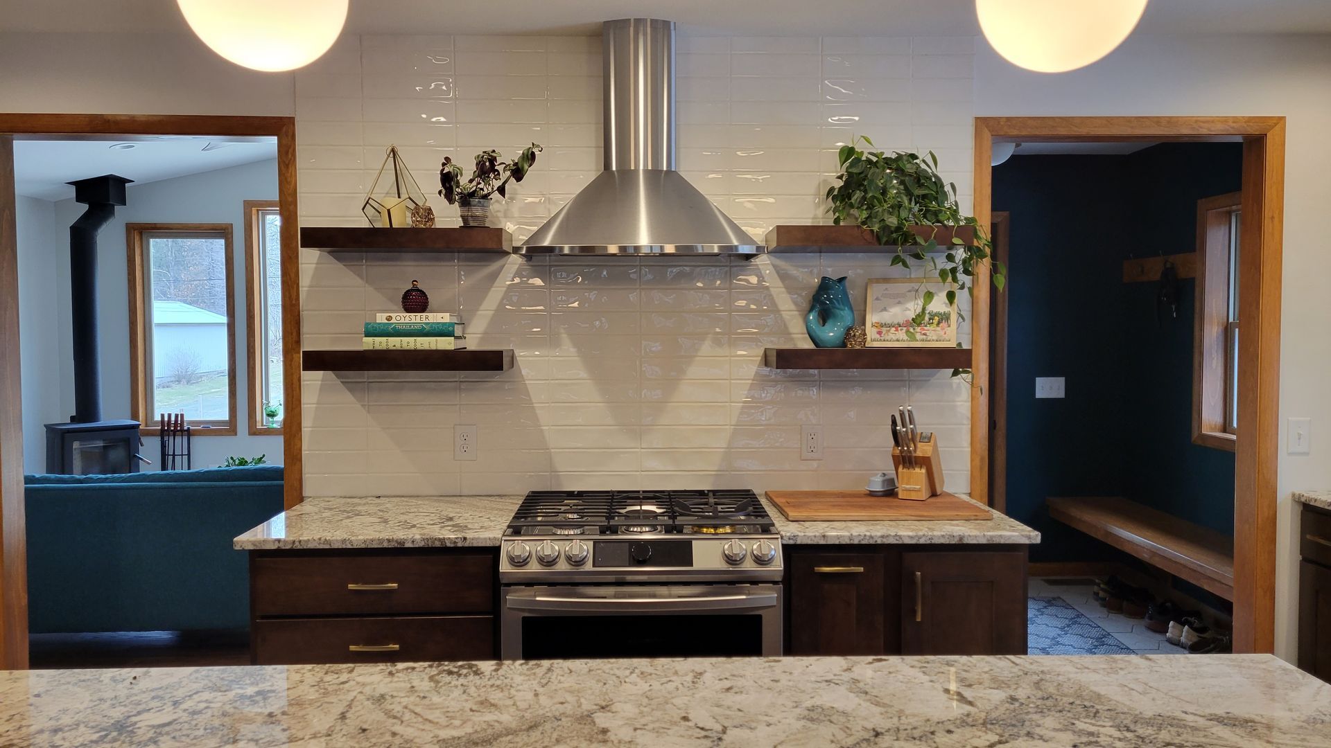 Kitchen with stove, stainless hood, granite countertops, wood cabinets, floating shelves, and two doorways.