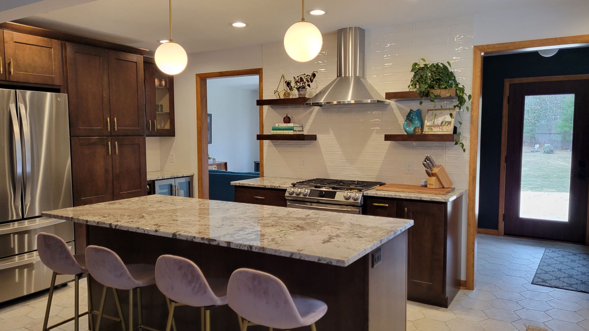 Modern kitchen with dark brown cabinets, granite island, and light pink stools; globe pendant lights.
