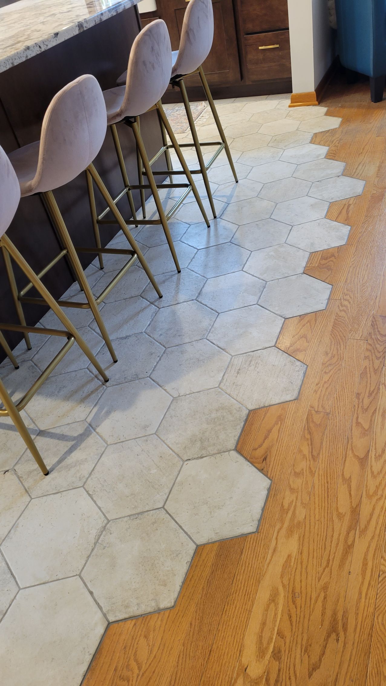 Hexagon tile floor meets wood floor, with gold-legged bar stools at a countertop.