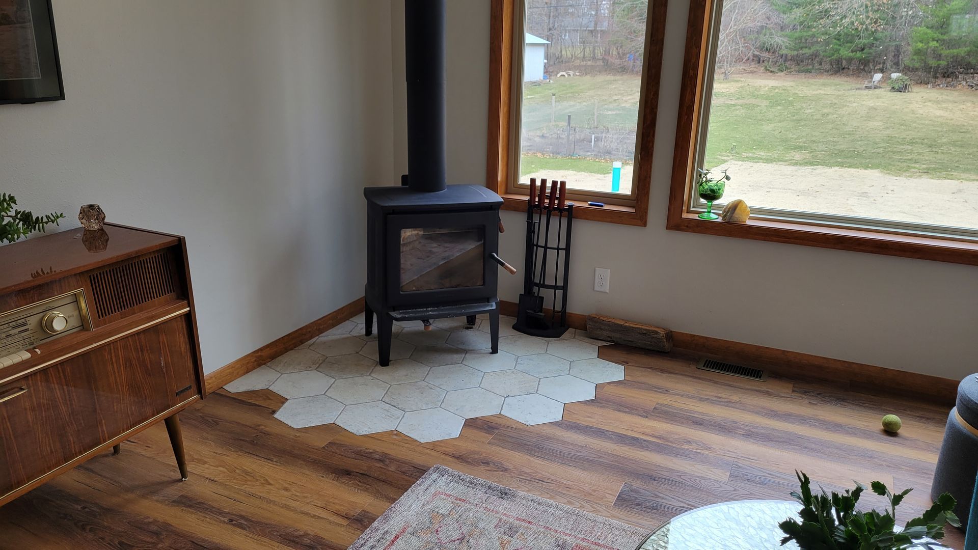 Cozy living room with a wood-burning stove, large window, and wooden floors.