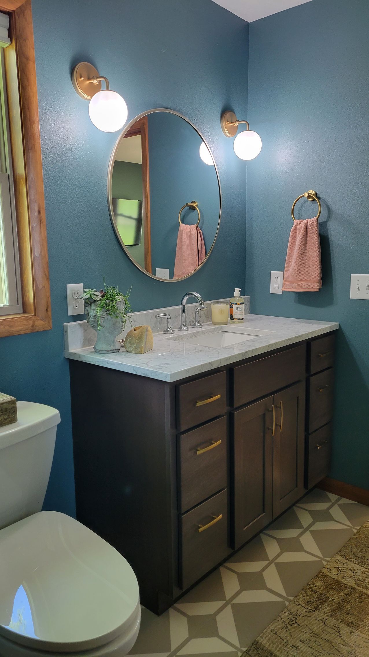 Bathroom with dark gray vanity, round mirror, blue walls, and patterned floor.