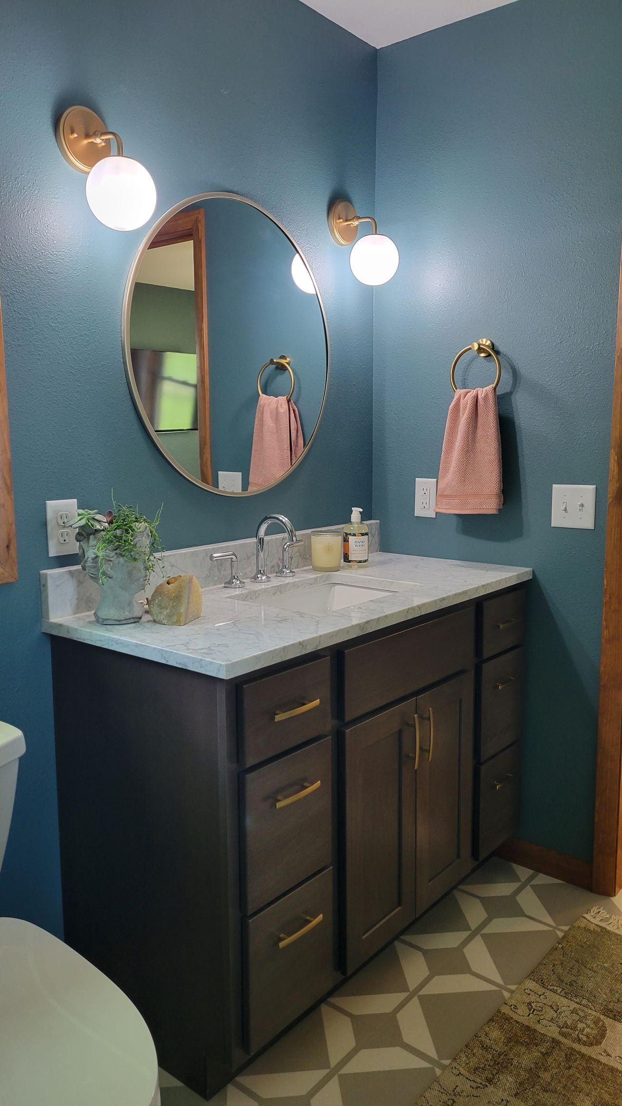 Bathroom with blue walls, a dark vanity, round mirror, and gold fixtures.