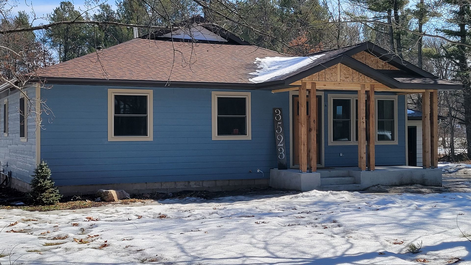 Blue house with new wooden porch under construction, snowy ground.