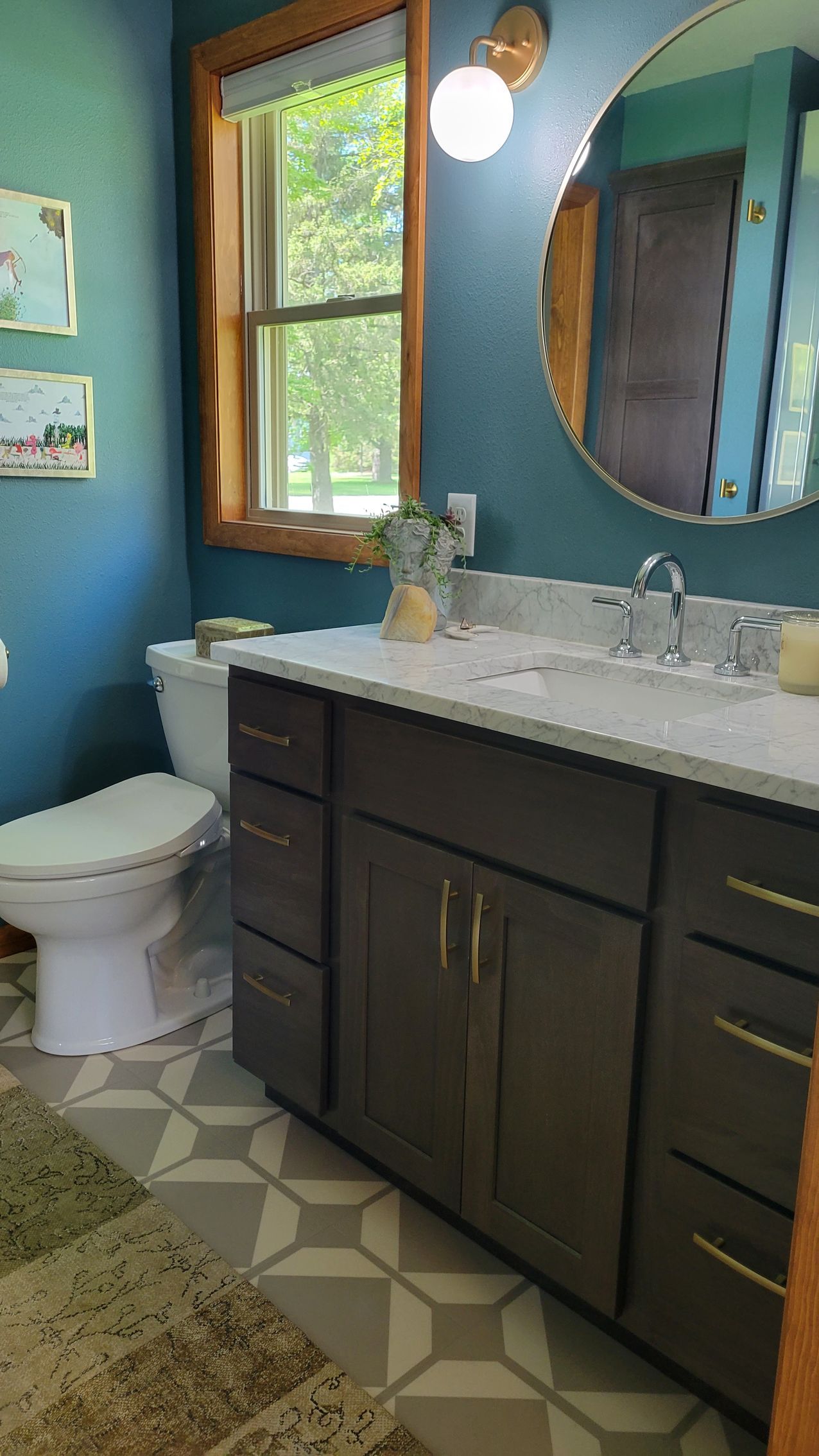 Bathroom with teal walls, a dark brown vanity, and a large round mirror.