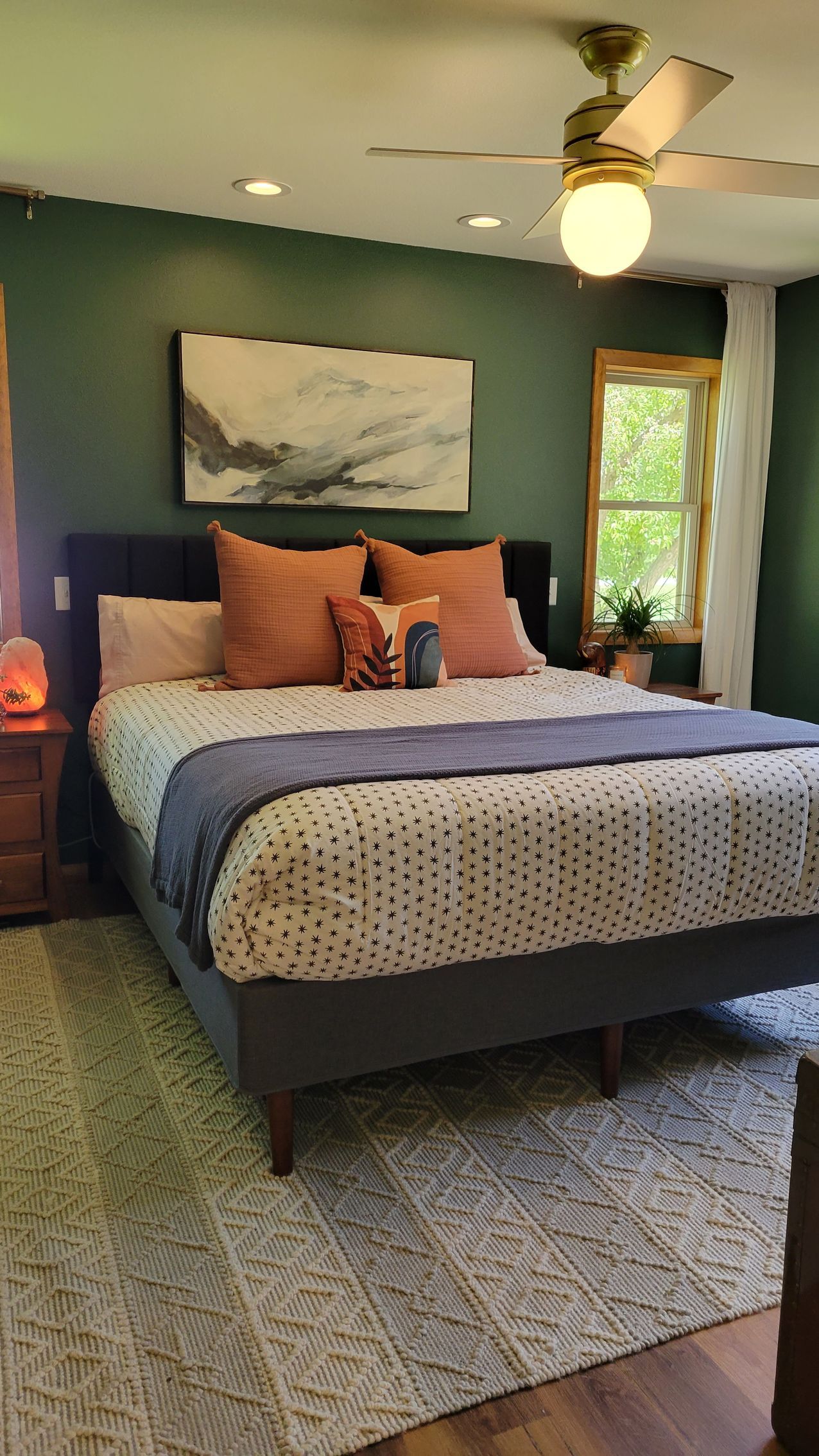Bedroom with a king-sized bed, green walls, rug, art, and a ceiling fan.