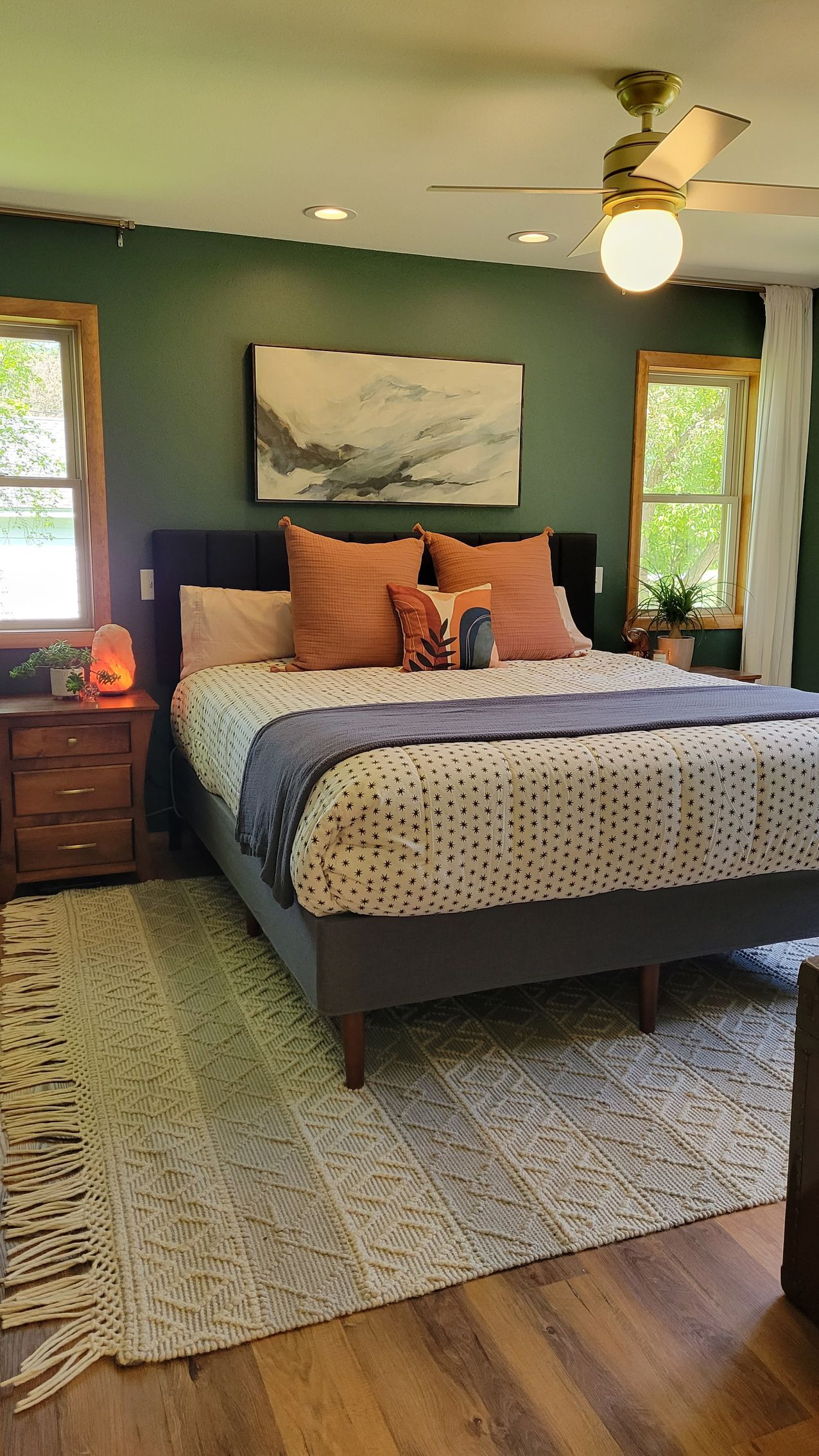 Bedroom with dark green walls, a bed with orange pillows, and a patterned rug.