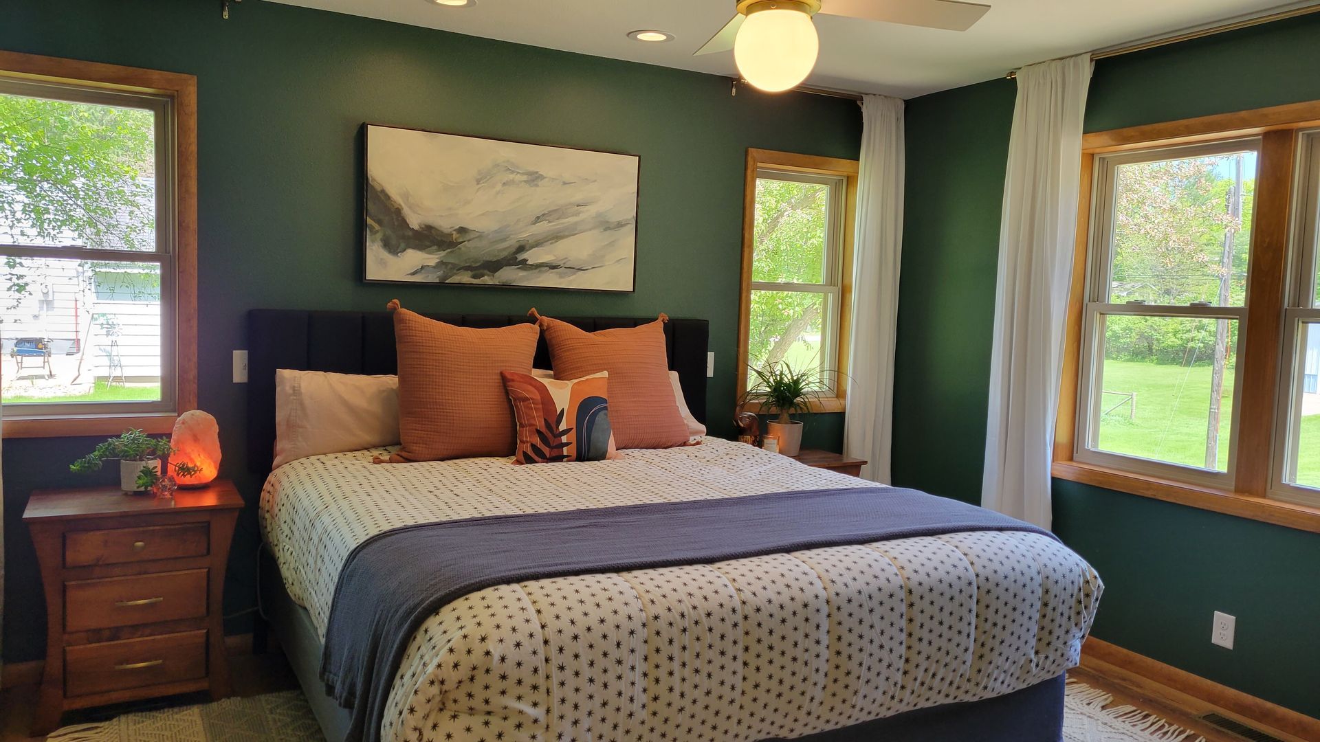 Green bedroom with bed, artwork, and windows.