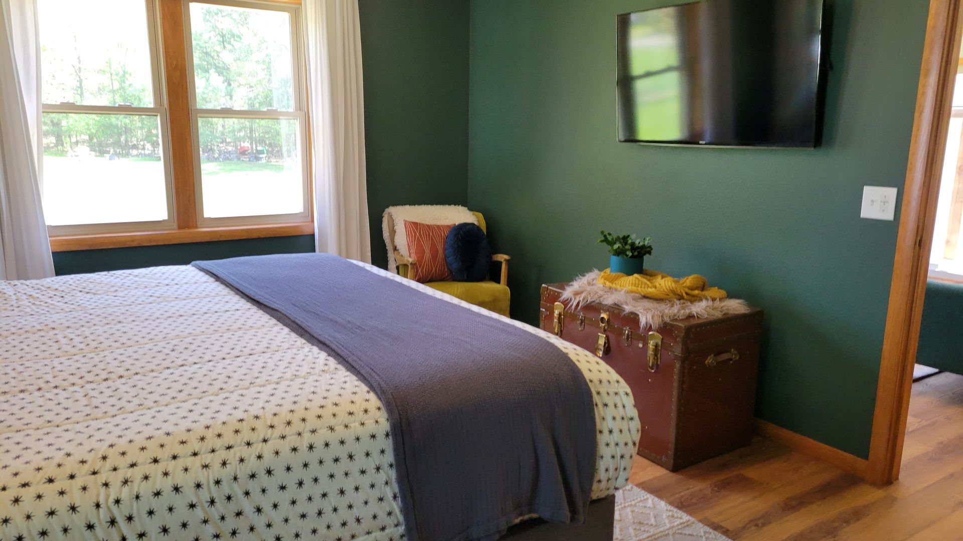 Bedroom with bed, trunk, chair, TV, green walls, and window.