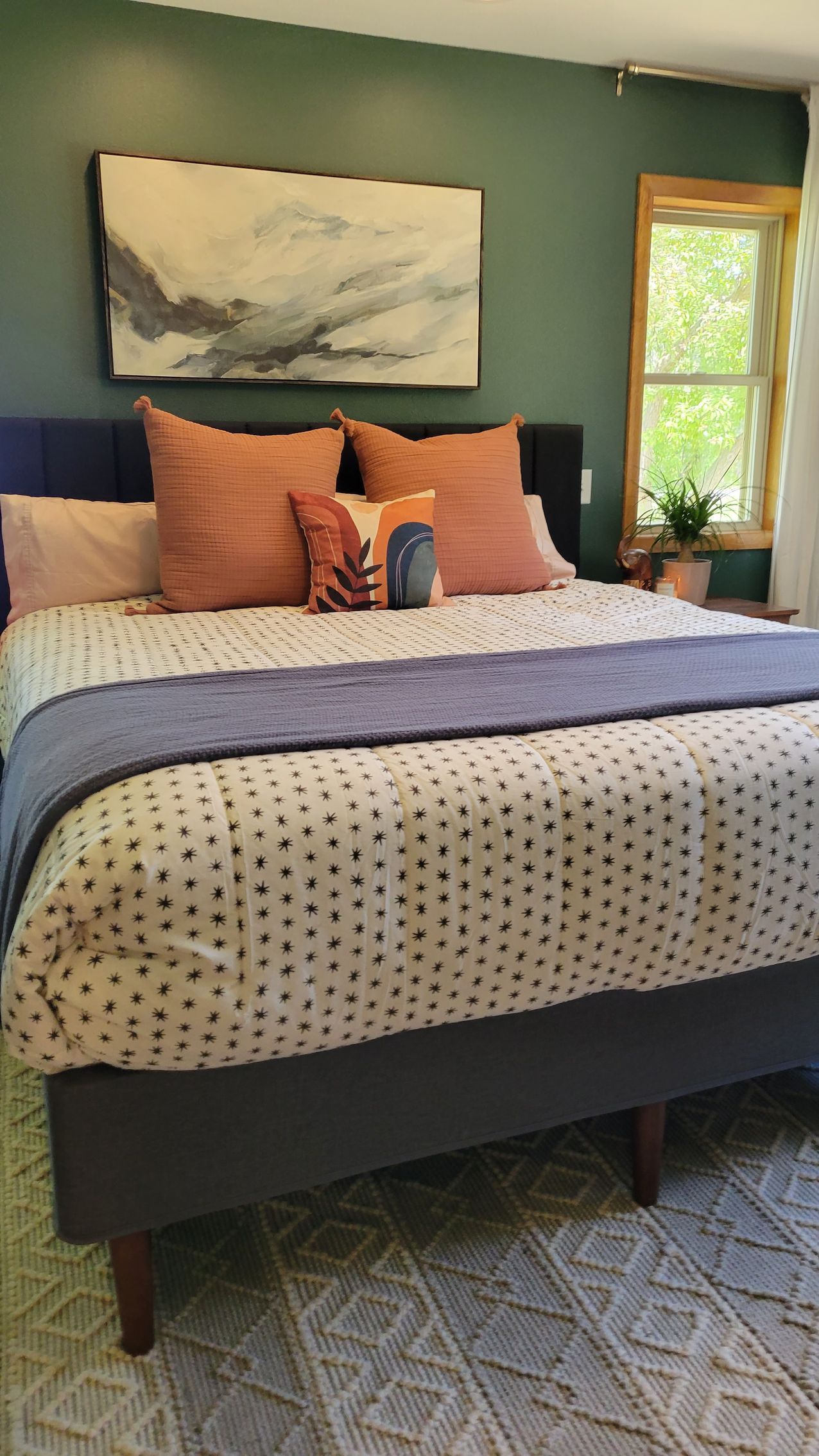 Bedroom with bed, teal wall, art, orange and blue pillows, and patterned bedding.