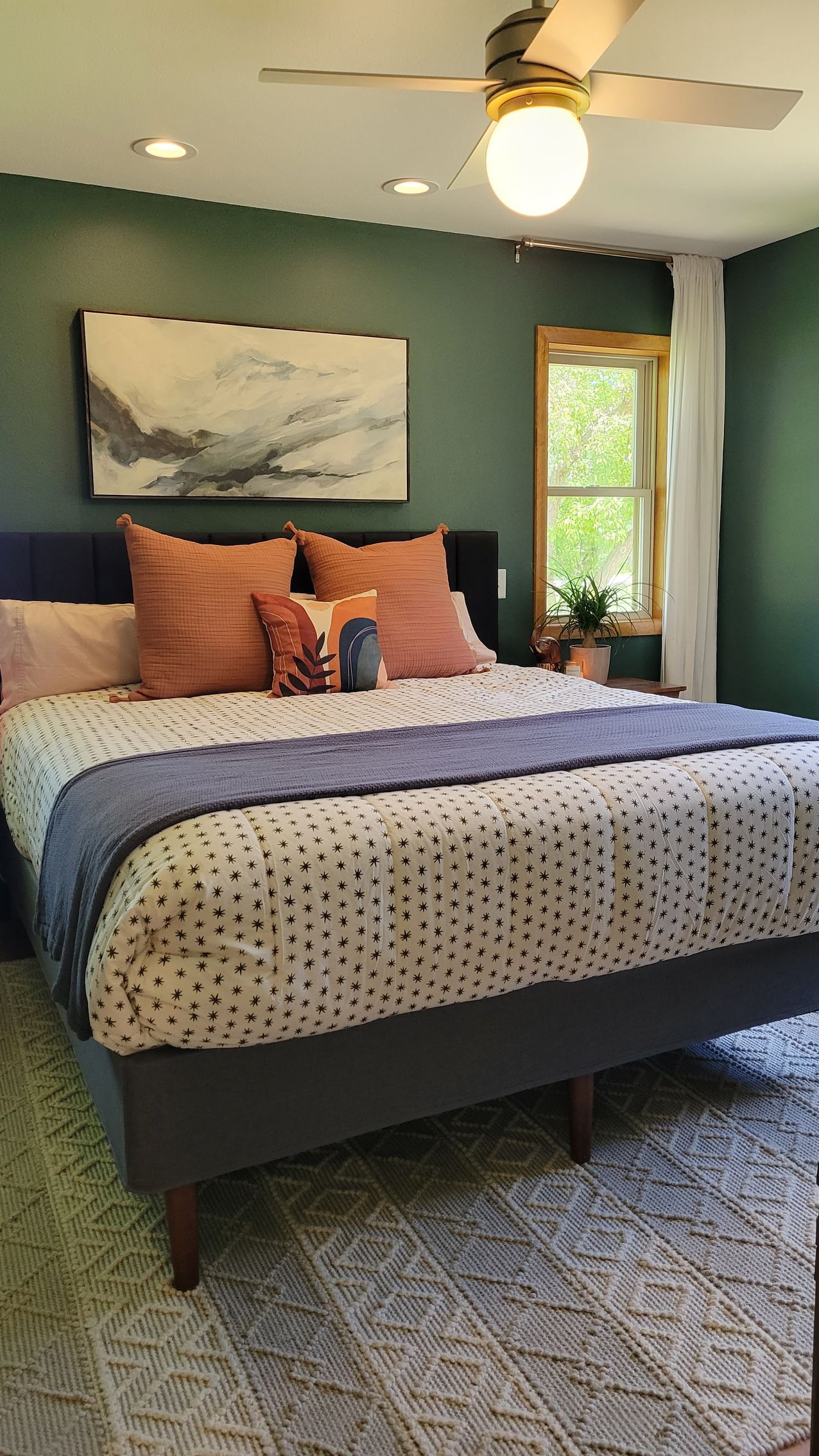 Bedroom with green walls, a bed with coral and blue accents, and a large abstract artwork.