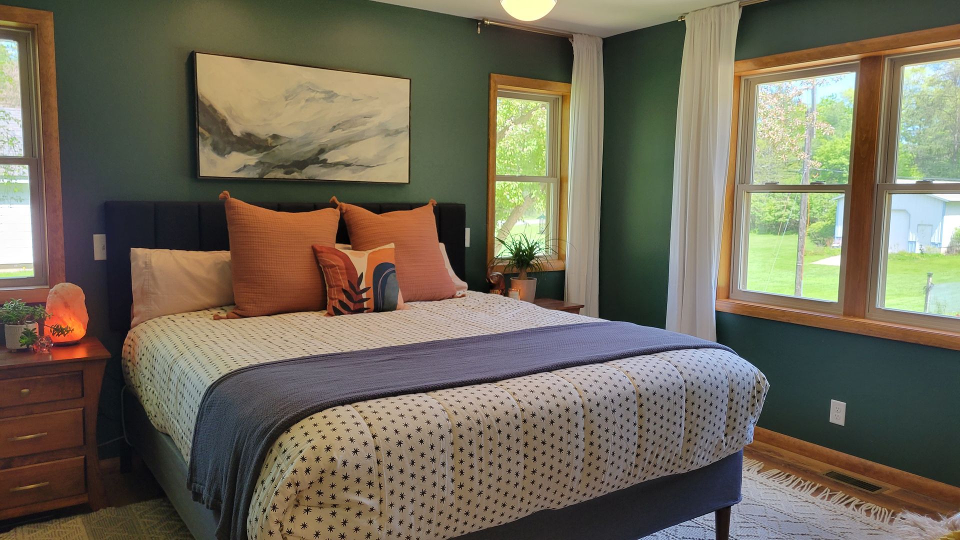 Cozy bedroom with green walls, wooden trim, and bed with orange, gray, and white patterned bedding.