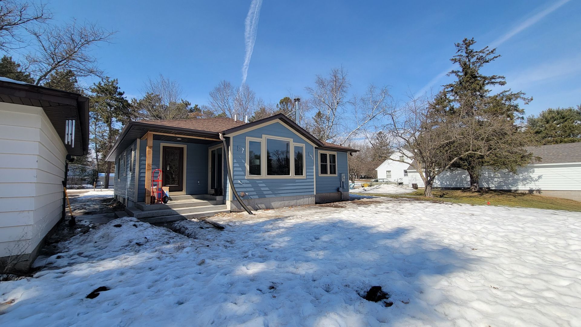 Blue house with snow on the ground, trees and a blue sky in the background.