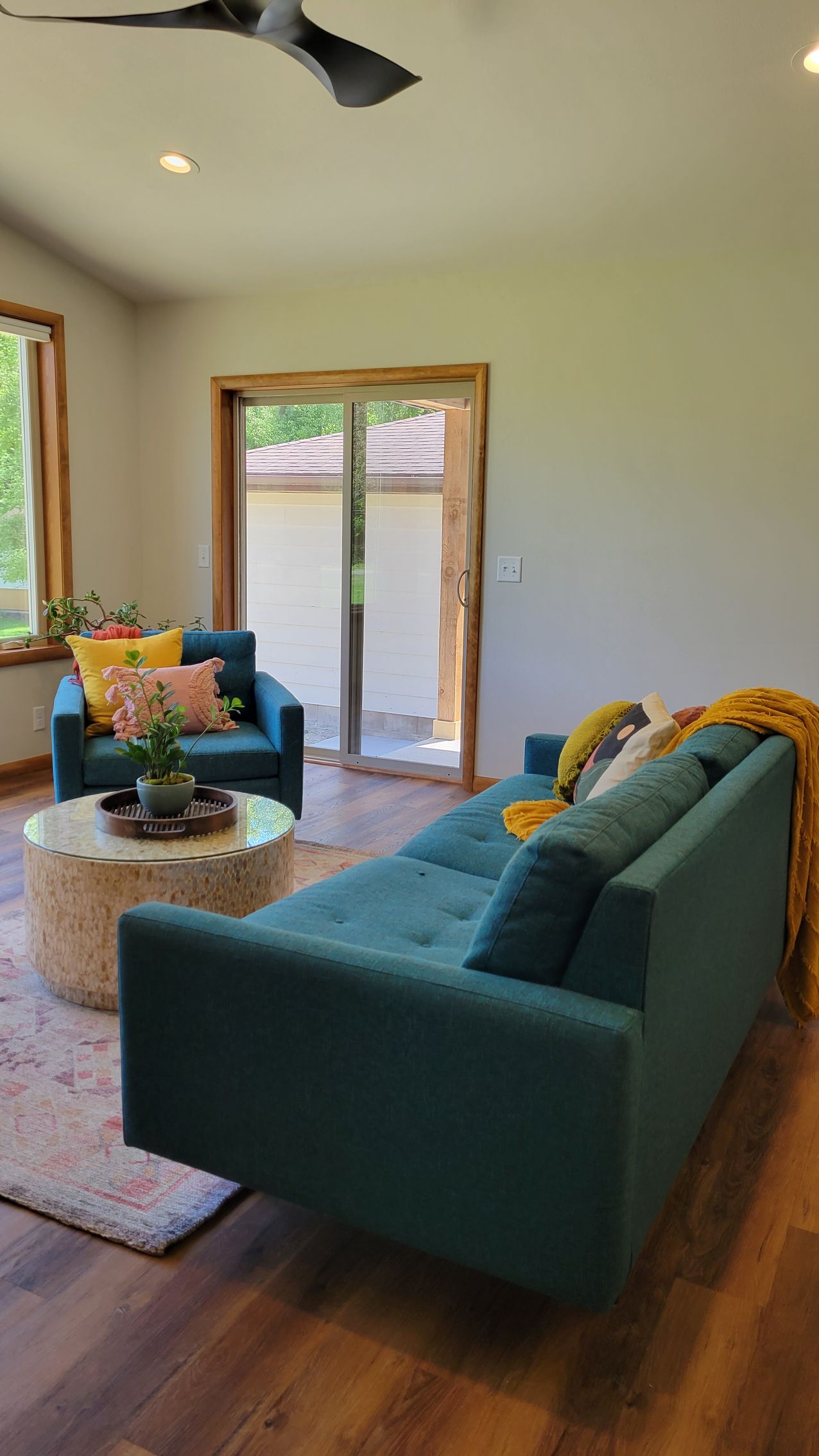Teal sectional and armchair in living room with a round coffee table and sliding glass door.
