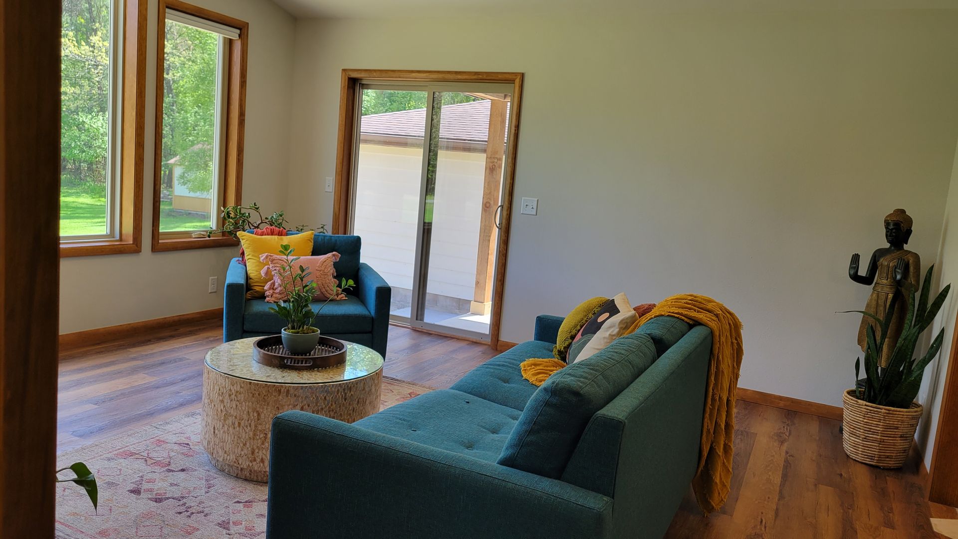 Living room with teal sofa and armchair, round coffee table, sliding door, and a wooden framed window.