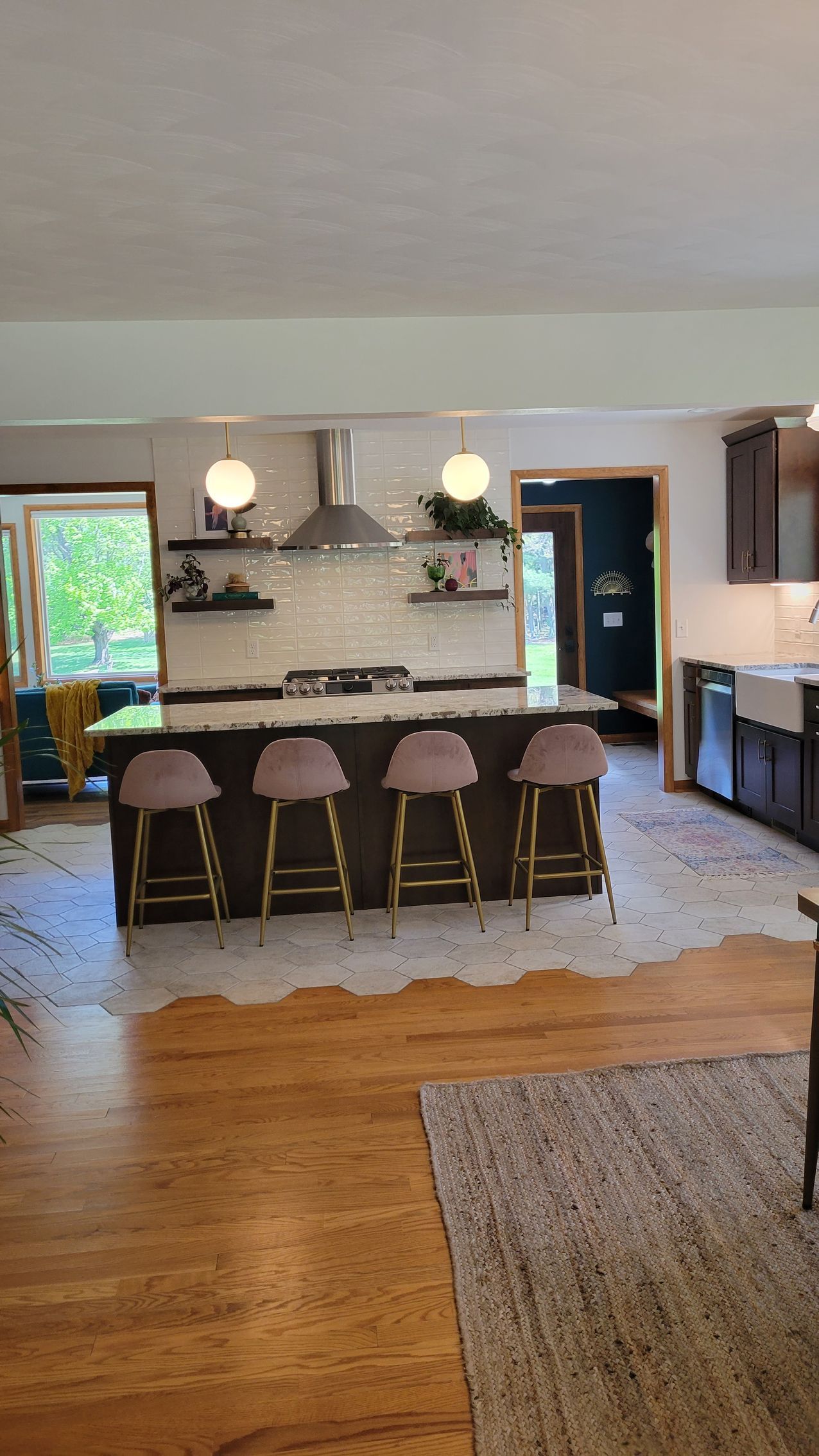 Kitchen with island, bar stools, and hardwood floors. Brown cabinets, white backsplash, and decorative lighting.