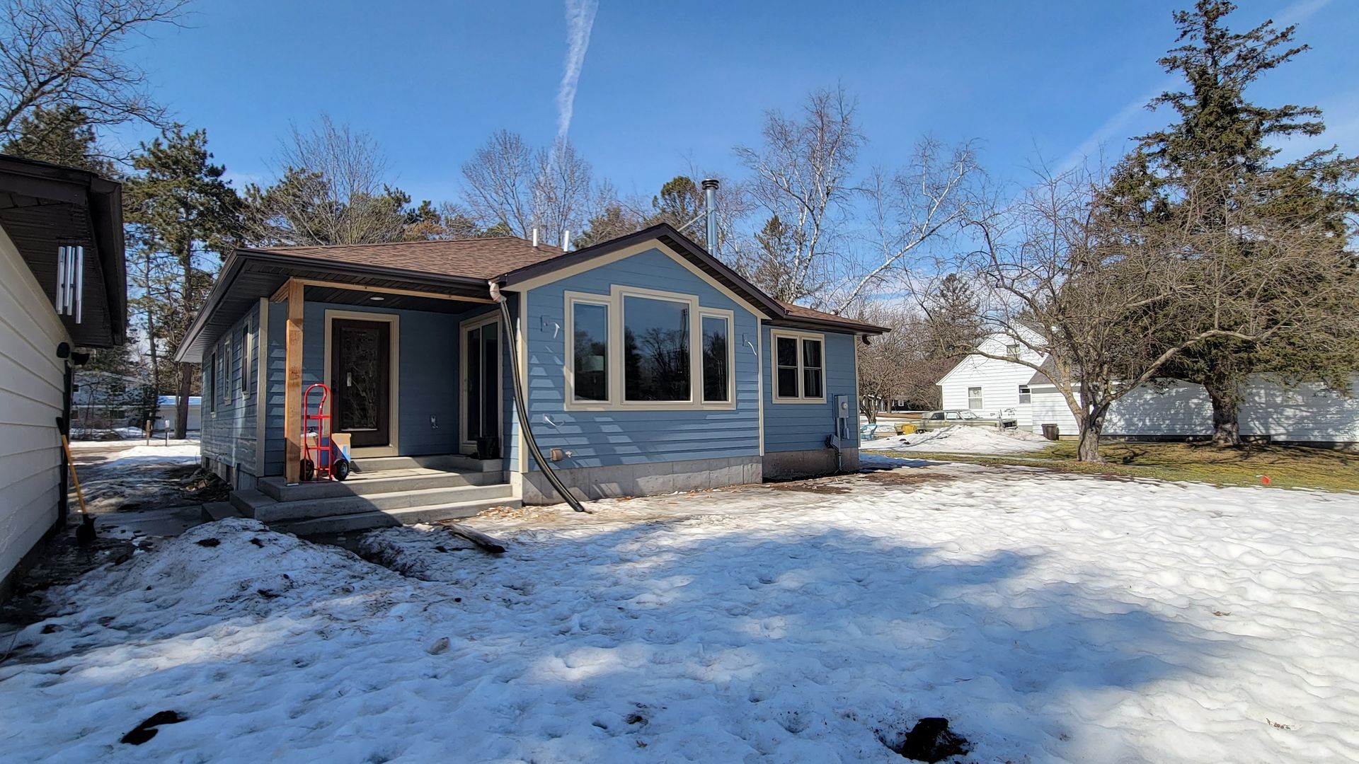 Blue house with snow-covered yard, clear sky. Trees surround the house.
