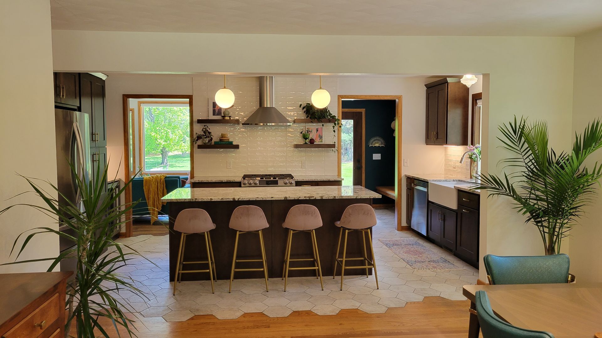 Kitchen with island, dark cabinets, light tile floor. Pink bar stools, stainless steel appliances, plants.